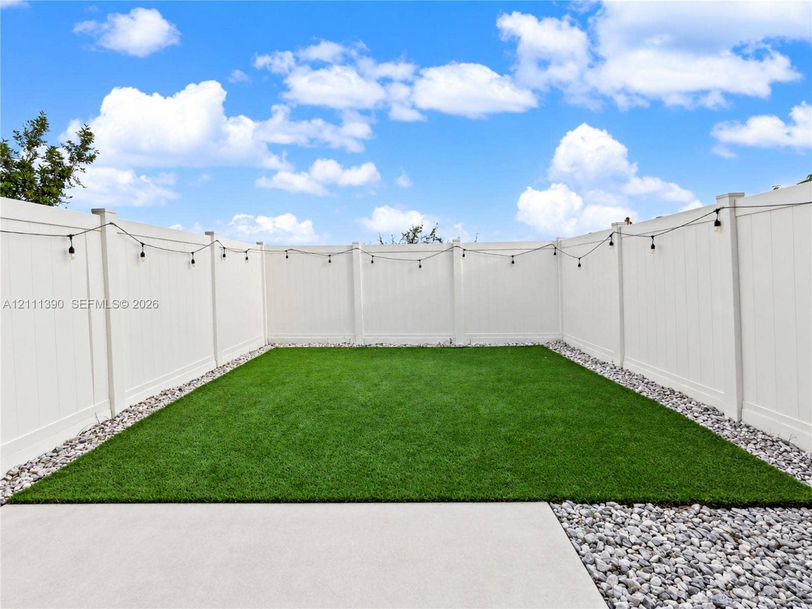 1074 NW 6th Terrace, Florida City, Florida City, FL 33034 Enclosed backyard featuring a white vinyl privacy fence, synthetic turf lawn, concrete patio, and gravel borders