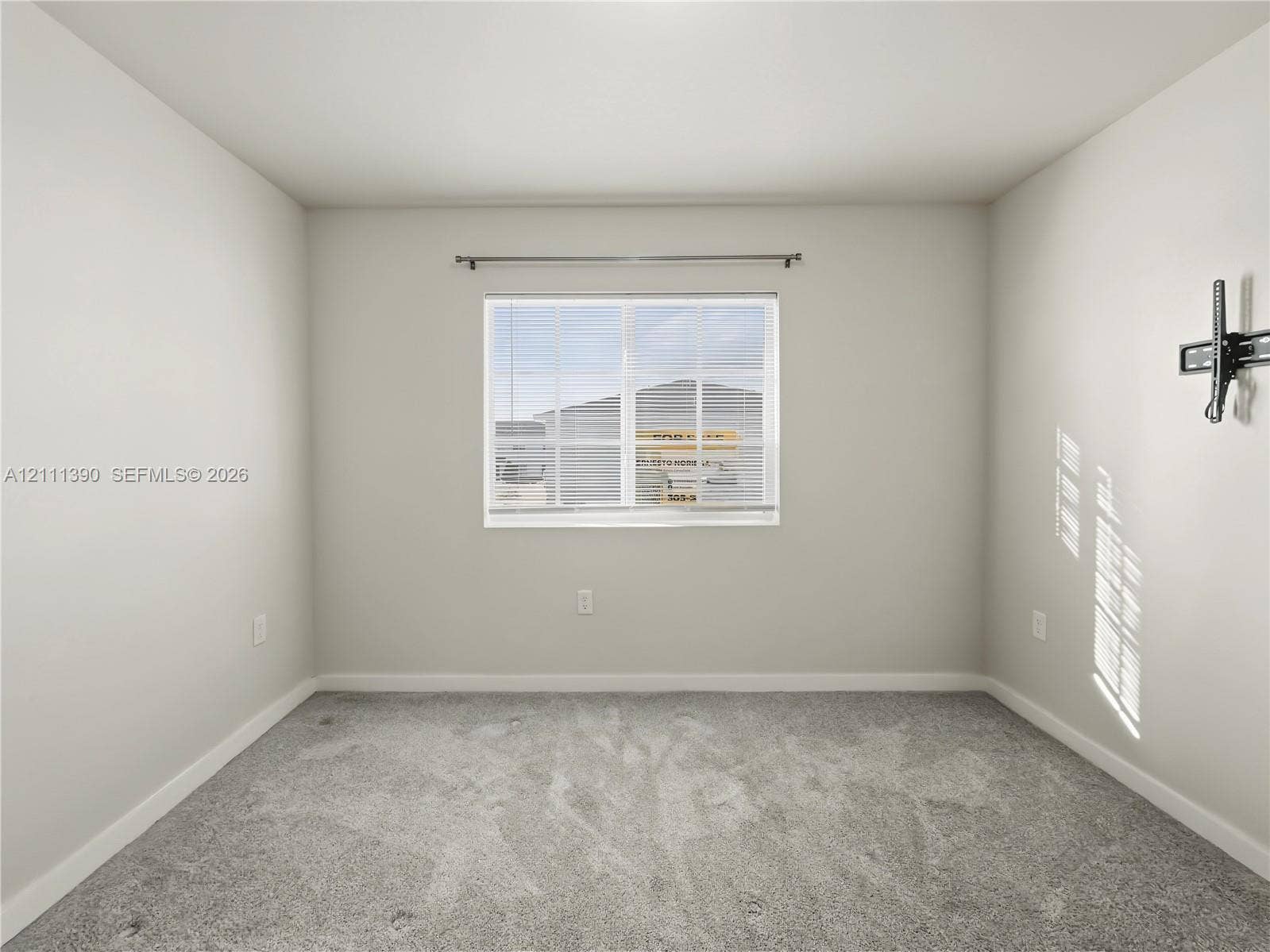 1074 NW 6th Terrace, Florida City, Florida City, FL 33034 Neutral-toned interior room featuring wall-to-wall carpeting, a horizontal sliding window with attached curtain rod, and a wall-mounted television bracket