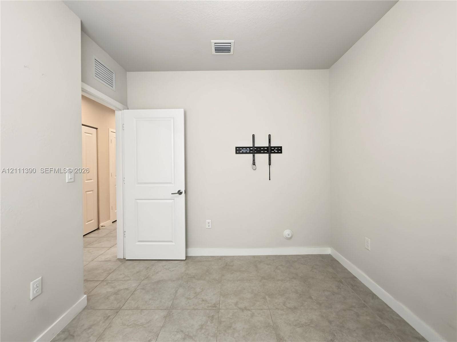 1074 NW 6th Terrace, Florida City, Florida City, FL 33034 Neutral-toned interior space featuring light-colored tile flooring, smooth wall finishes, a solid-core interior door, and a wall-mounted display bracket