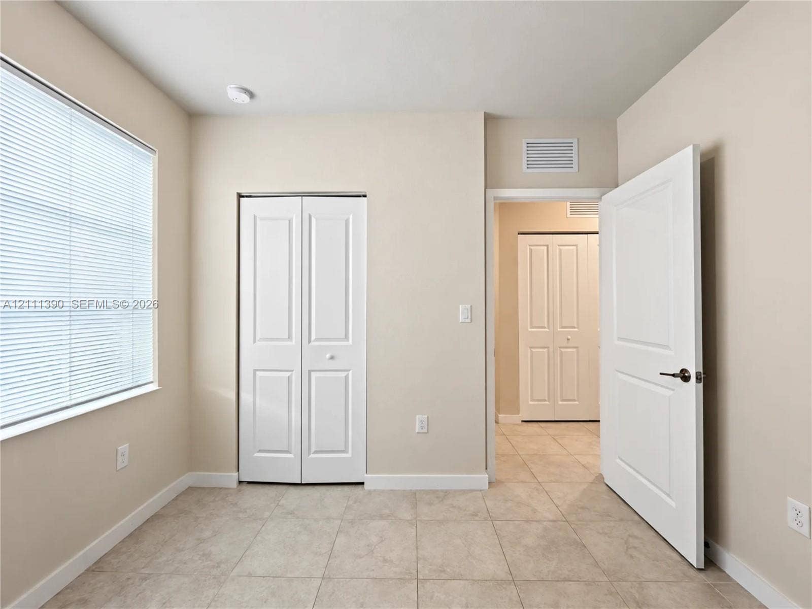 1074 NW 6th Terrace, Florida City, Florida City, FL 33034 Neutral-toned room featuring tile flooring, a window with horizontal blinds, and two sets of white panel doors