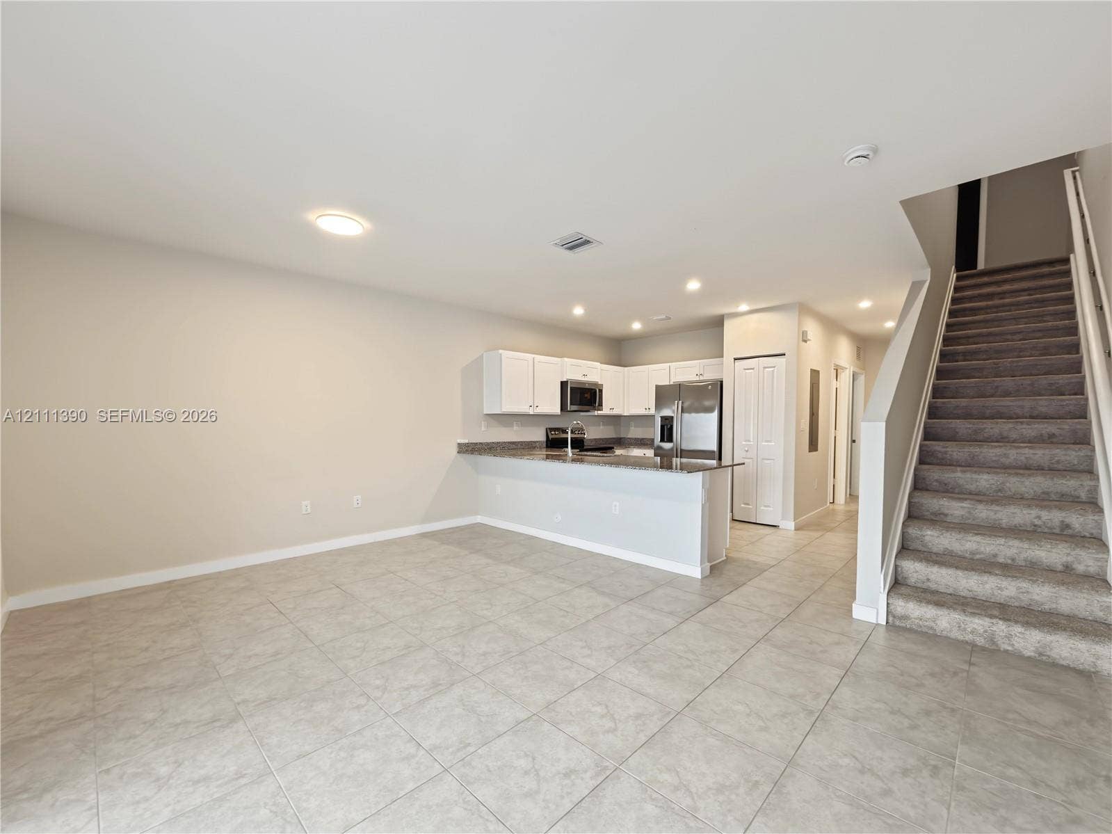 1074 NW 6th Terrace, Florida City, Florida City, FL 33034 Open-concept kitchen featuring white cabinetry, stone-finish countertops, stainless steel appliances, and tile flooring, with carpeted stairs