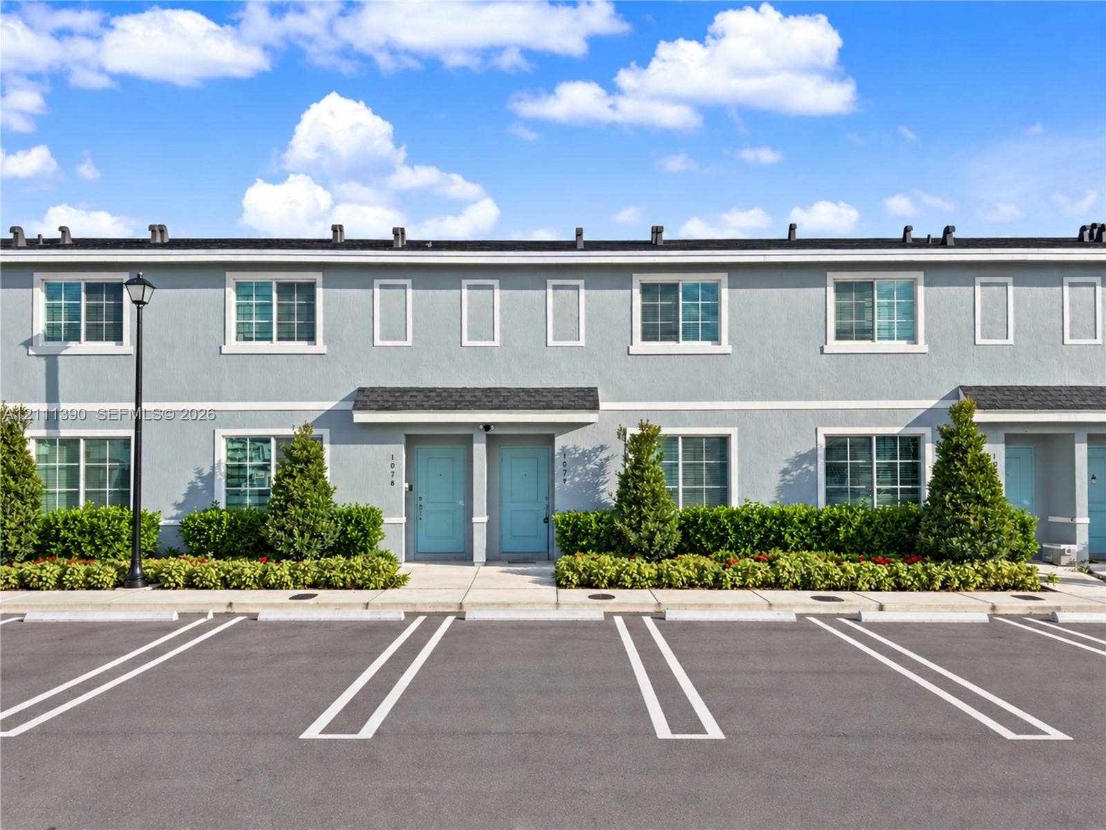 1074 NW 6th Terrace, Florida City, Florida City, FL 33034 Two-story multi-unit exterior featuring smooth grey stucco facade, dark asphalt shingle roof, dual light-blue entry doors, and dedicated paved parking stalls