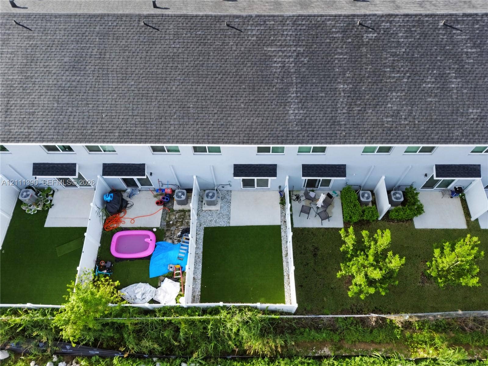 1074 NW 6th Terrace, Florida City, Florida City, FL 33034 Aerial perspective of townhome exteriors featuring low-maintenance artificial turf lawns, concrete patios, and white vinyl privacy fencing