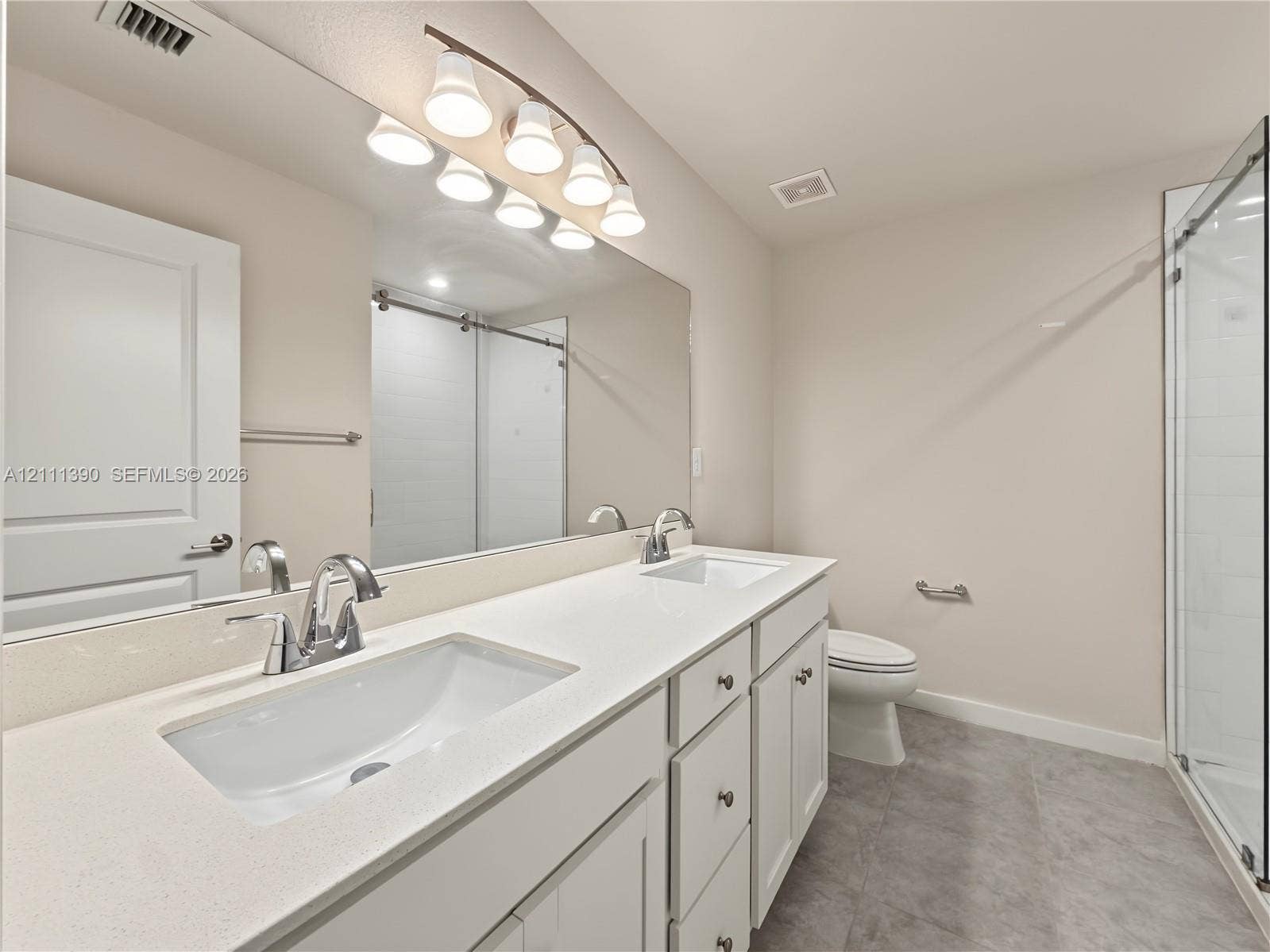 1074 NW 6th Terrace, Florida City, Florida City, FL 33034 Dual-sink vanity with white cabinetry, light-toned stone countertops, polished chrome fixtures, full-width mirror, and a glass-enclosed shower