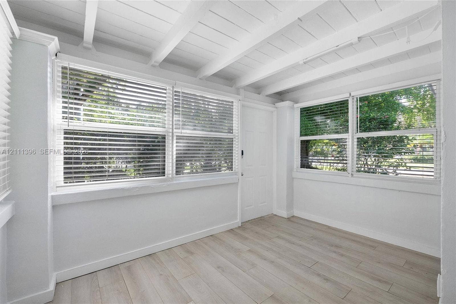 Exposed beamed ceiling with white finish, wood-finish flooring, and multiple large windows with horizontal blinds