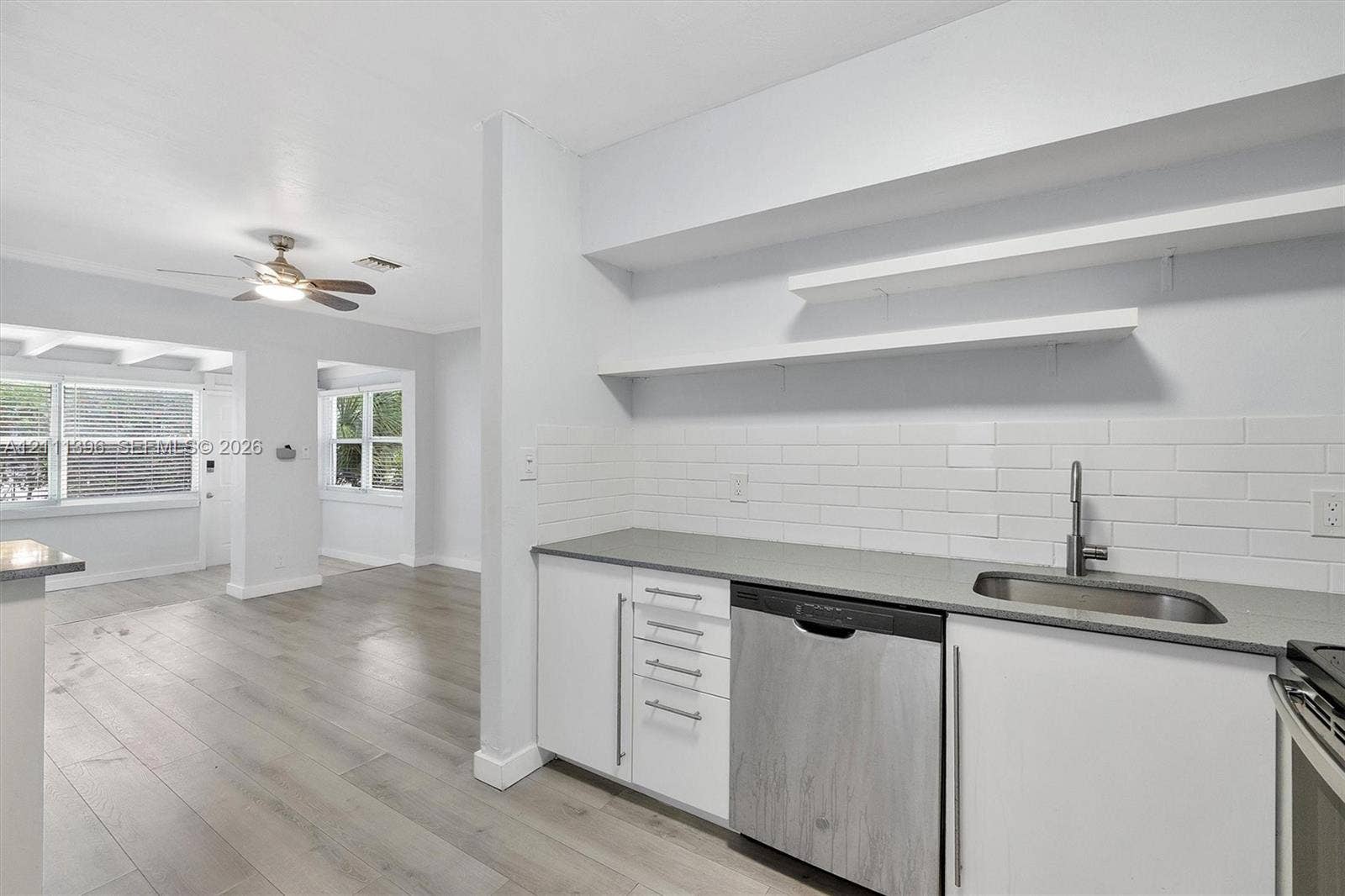 Kitchen featuring white flat-panel cabinetry, light-toned countertops, subway tile backsplash, stainless steel dishwasher, and open shelving
