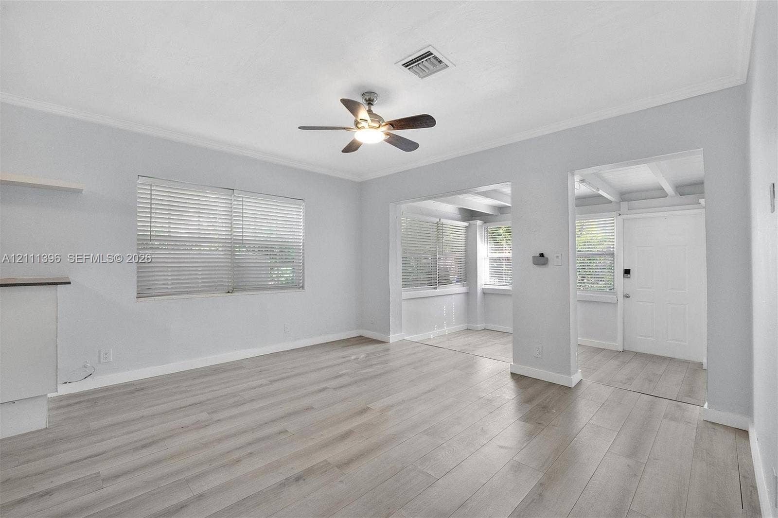 Interior space featuring neutral wall paint, wood-finish flooring, a ceiling fan with integrated lighting, and multiple windows with horizontal blinds