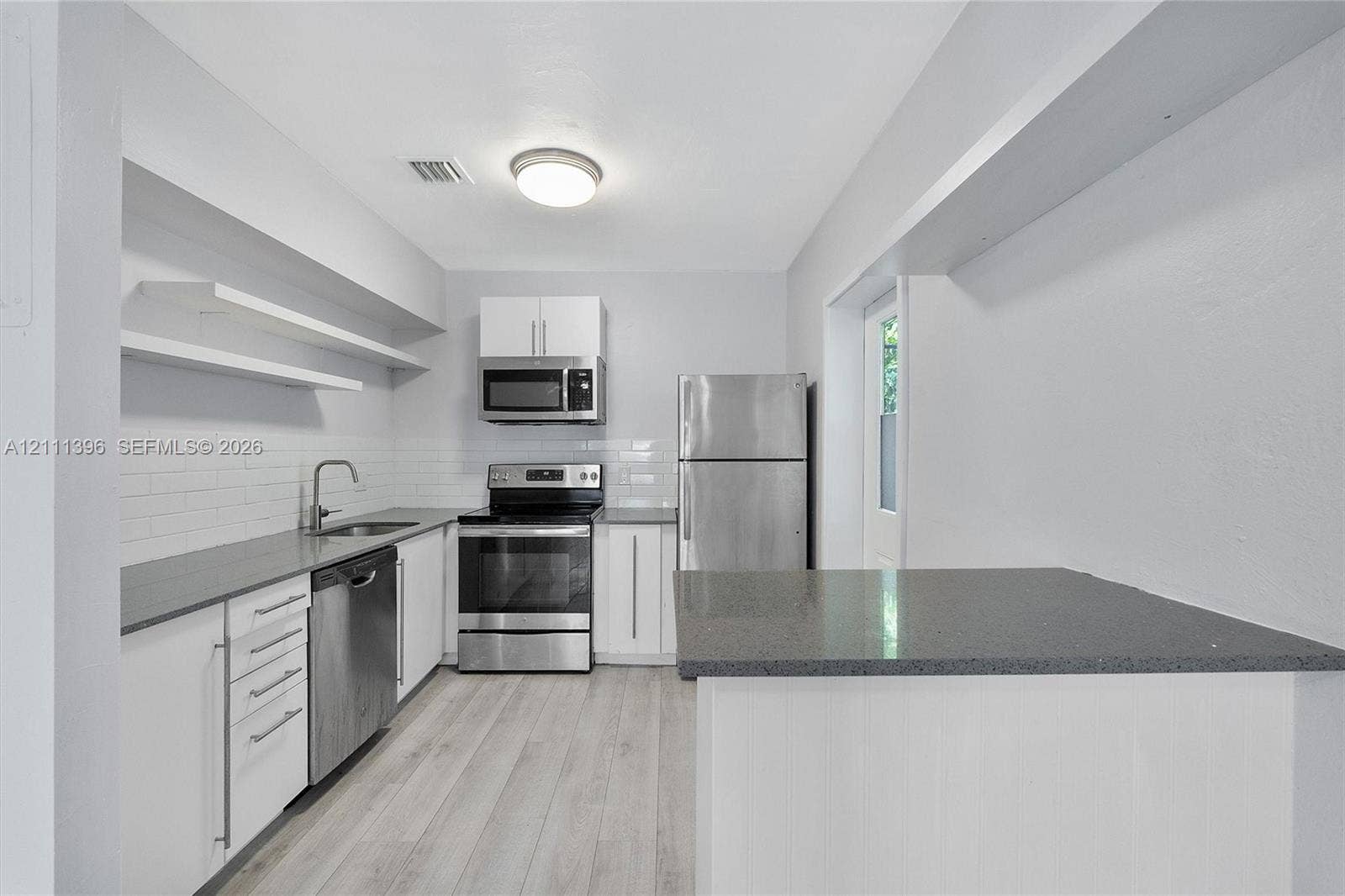Kitchen featuring white cabinetry, solid-surface countertops, subway tile backsplash, stainless steel appliances, and wood-finish flooring