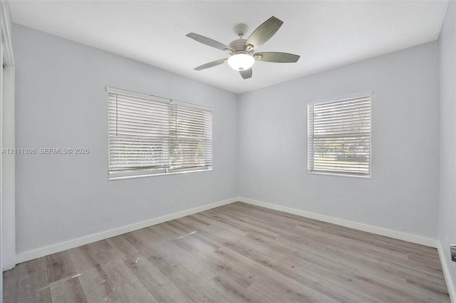 Wood-finish flooring, neutral wall tones, multi-blade ceiling fan with integrated light fixture, and horizontal window blinds