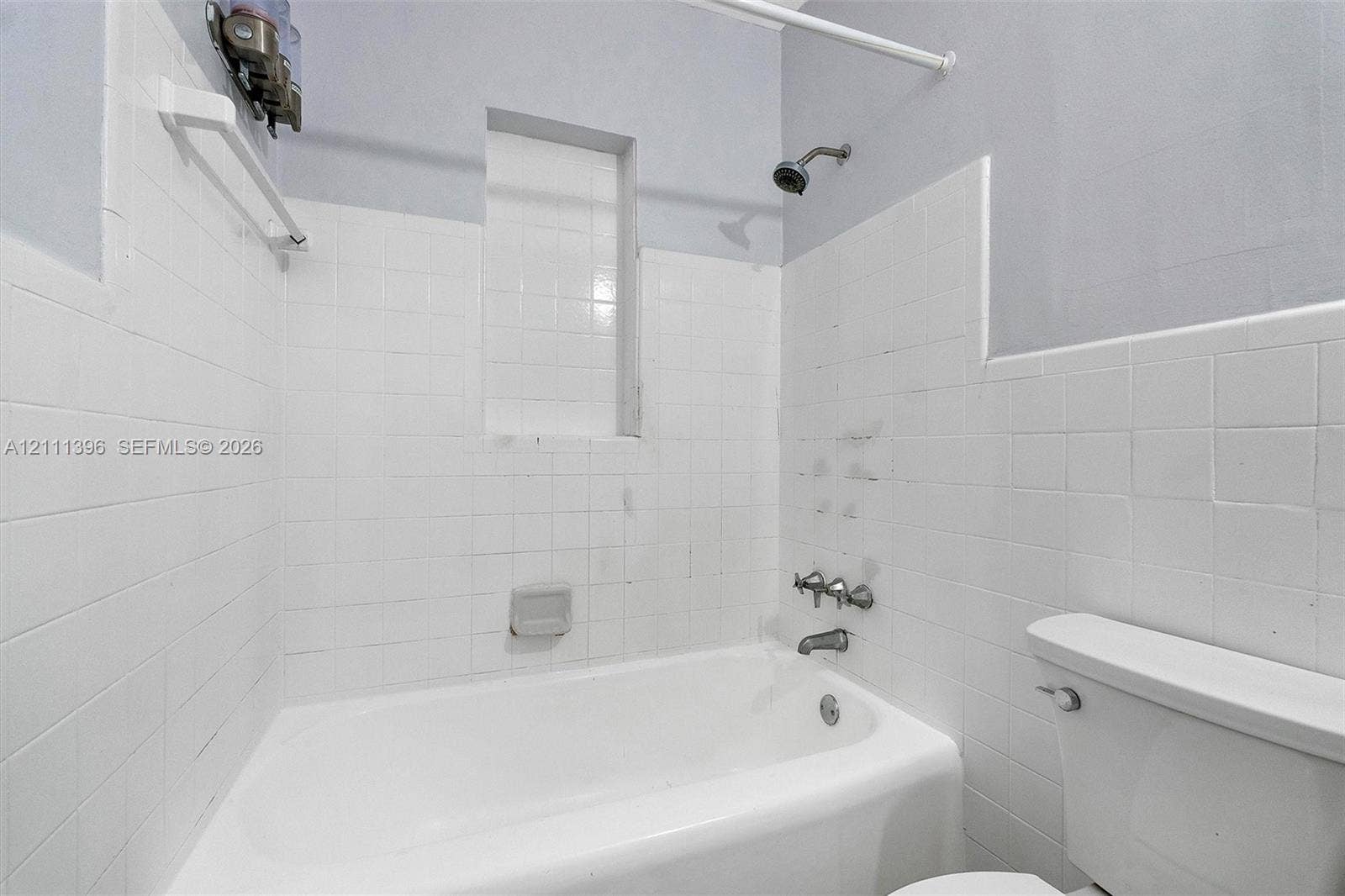 Bathroom featuring a white porcelain tub, ceramic wall tiling, a built-in recessed shelf, and a dual-handle metal faucet