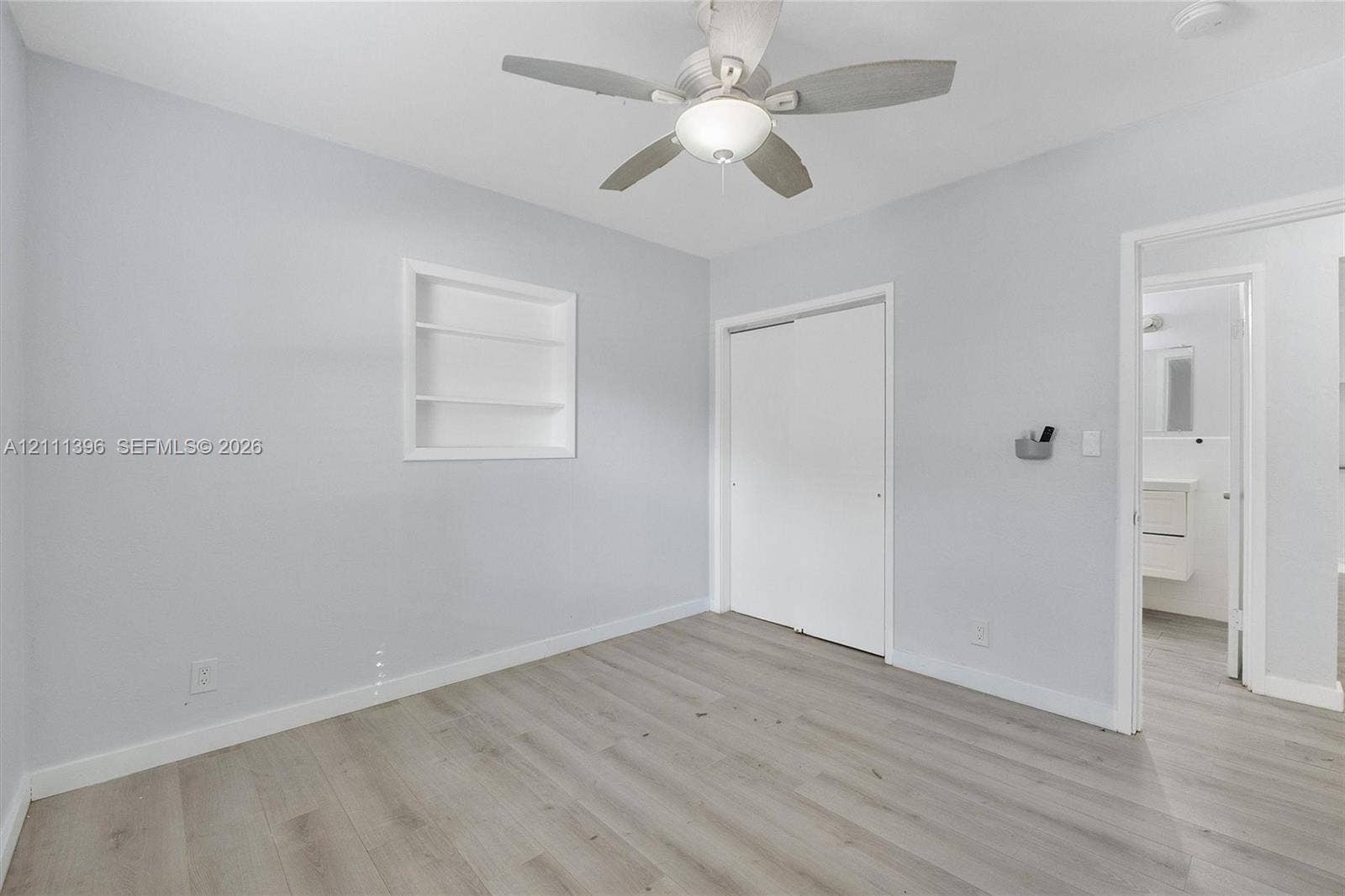 Neutral interior featuring wood-finish flooring, a ceiling fan with integrated lighting, a recessed wall niche, and sliding closet doors