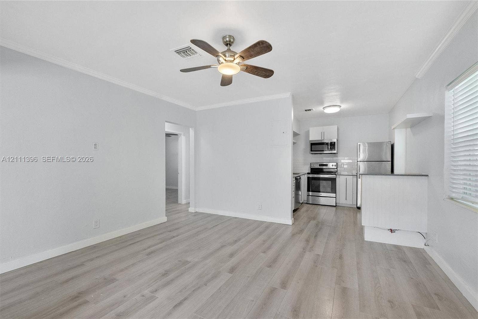Wood-finish flooring, central ceiling fan with integrated lighting, and kitchen featuring stainless steel appliances, crisp white cabinetry, and a peninsula counter