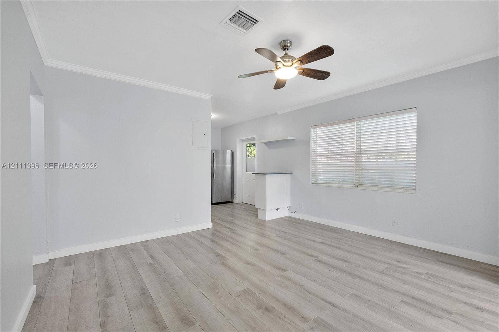 Neutral-toned room featuring wood-finish flooring, a ceiling-mounted fan with integrated lighting, horizontal window blinds, and a built-in counter surface