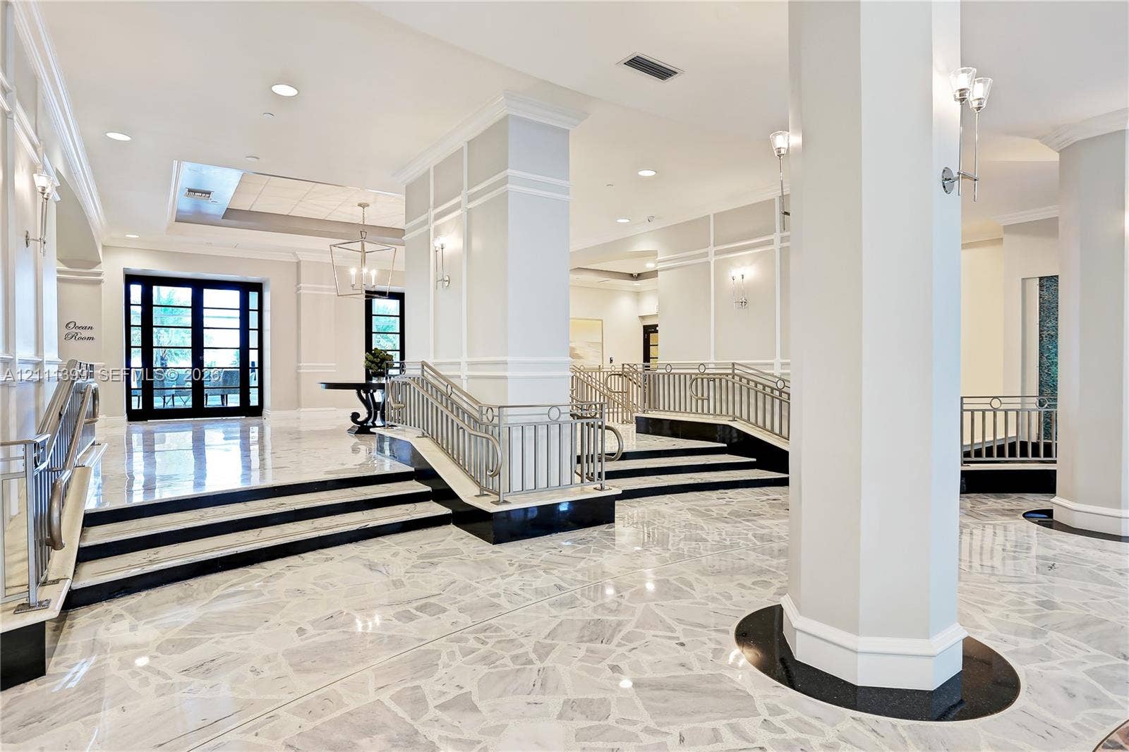 2501 S Ocean Drive, #1630, Hollywood, Hollywood, FL 33019 Grand foyer featuring polished stone flooring, custom wall millwork, tiered levels with dark stone accents, metallic railings, and decorative lighting fixtures