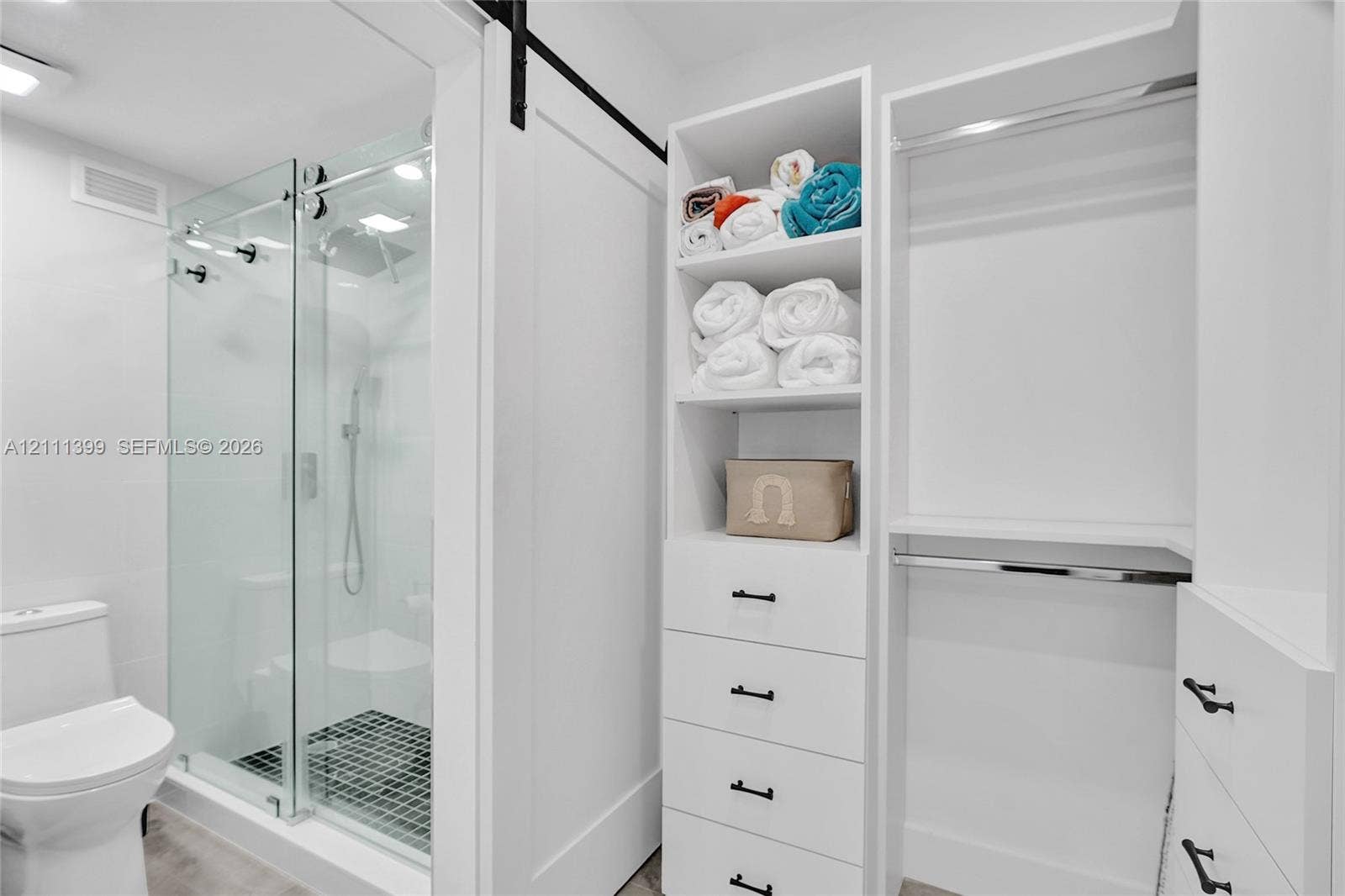 2501 S Ocean Drive, #1630, Hollywood, Hollywood, FL 33019 Walk-in shower with a glass enclosure and a black tiled floor, complemented by custom built-in cabinetry featuring white shelving, four storage drawers with matte black hardware, and an integrated hanging rod