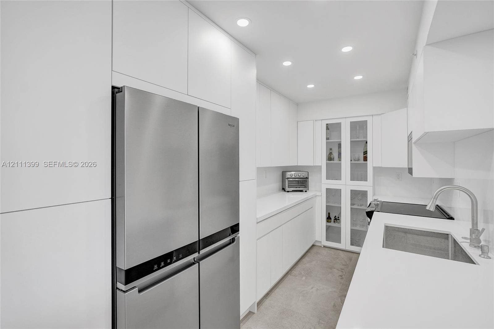 2501 S Ocean Drive, #1630, Hollywood, Hollywood, FL 33019 Contemporary kitchen featuring handleless white cabinetry, solid-surface countertops, integrated stainless steel appliances, built-in glass-front display cabinetry, and recessed lighting