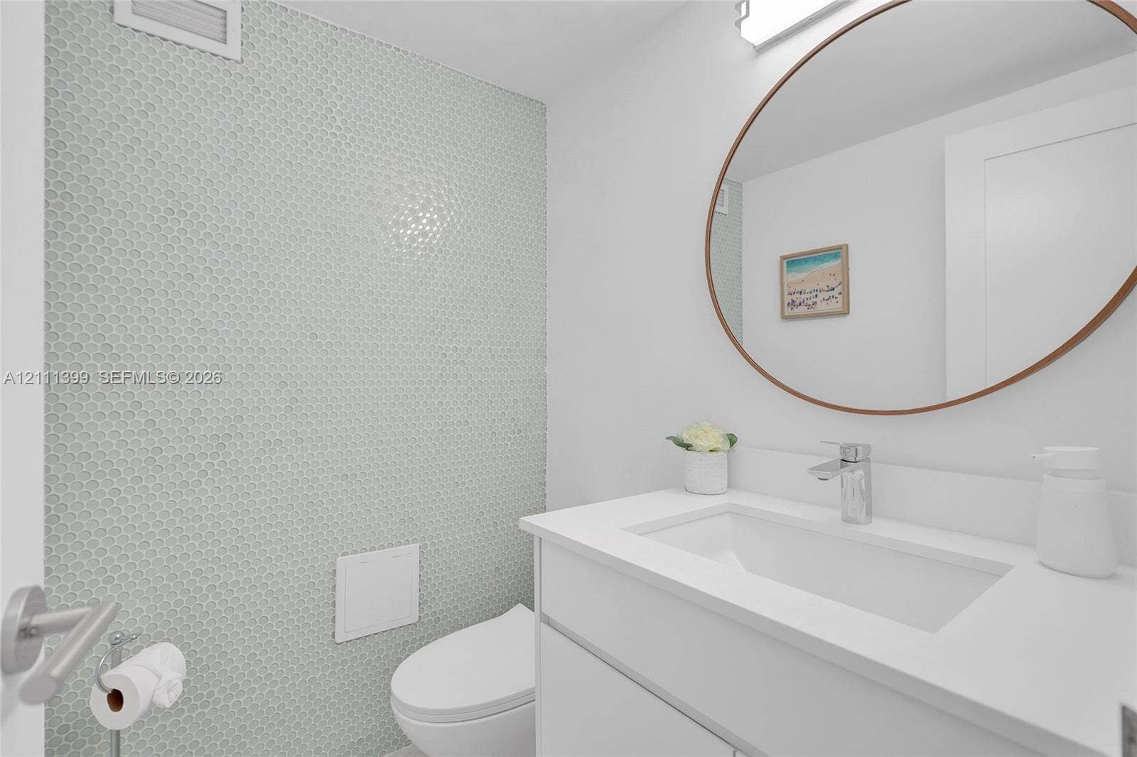 2501 S Ocean Drive, #1630, Hollywood, Hollywood, FL 33019 Modern vanity with integrated sink, quartz countertop, and polished chrome faucet, accented by a textured penny tile feature wall and a circular mirror with a bronze frame