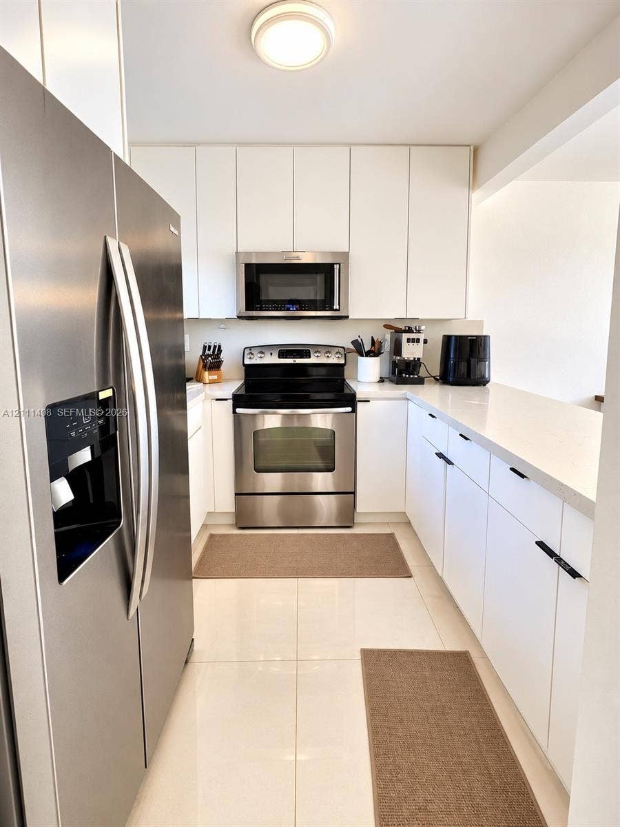 1700 N River Drive, #1004, Miami, FL 33125 Interior hallway featuring oversized floor tiles, white cabinetry with matte black hardware, and closet doors with louvered panels