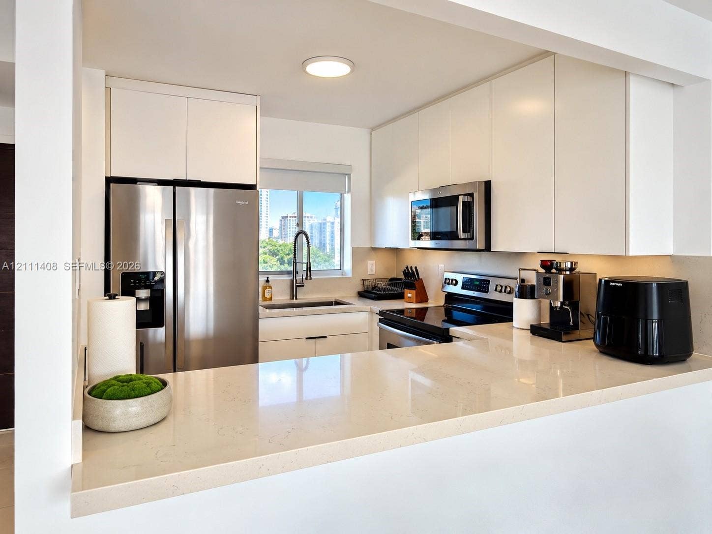 1700 N River Drive, #1004, Miami, FL 33125 Kitchen featuring white cabinetry, solid-surface countertops, tile flooring, and stainless steel appliances including a built-in microwave and refrigerator