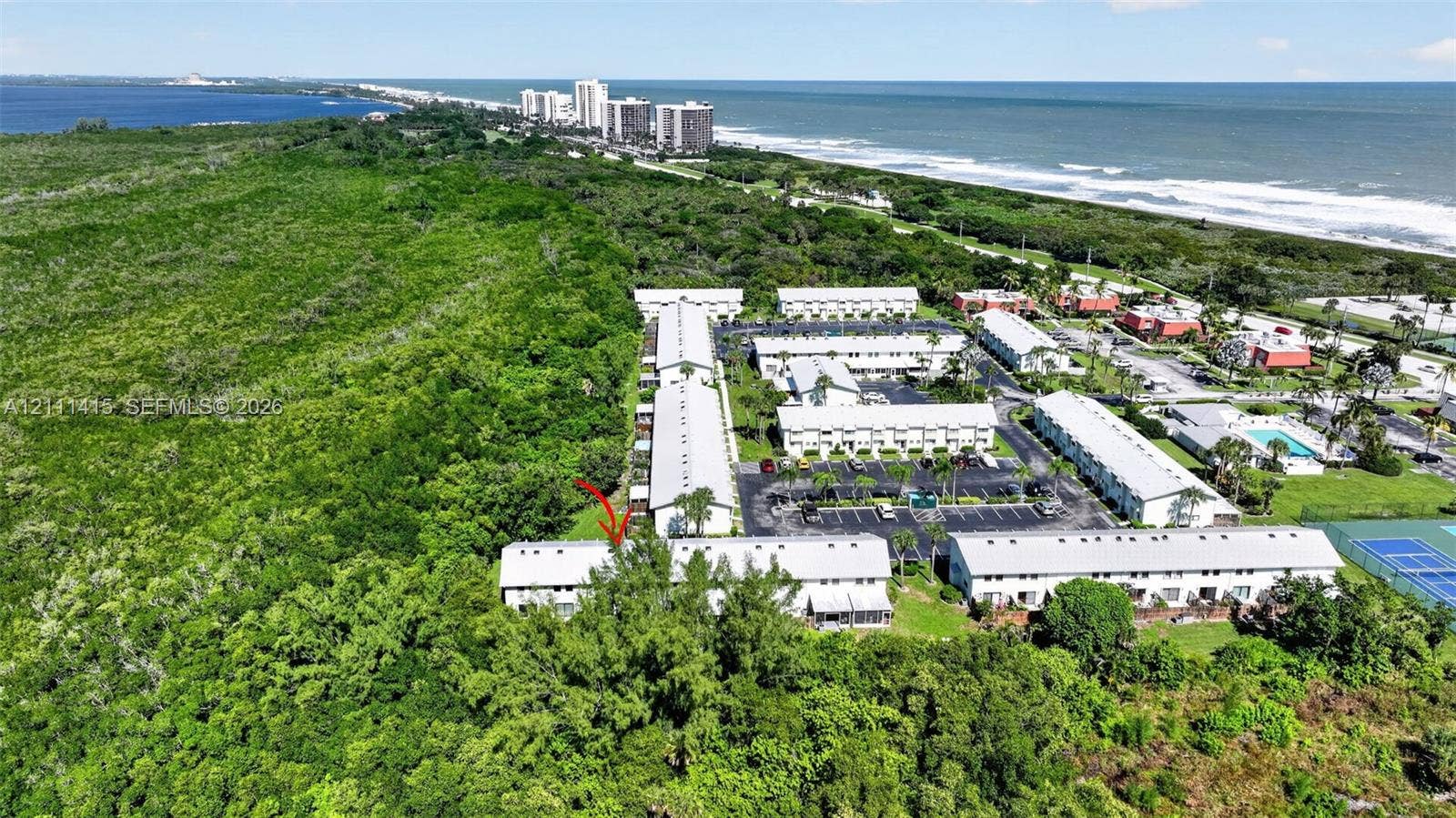 9423 S Ocean Drive, #80, Jensen Beach, FL 34957 Aerial perspective of multi-unit residential structures featuring light-colored shingled roofing, paved parking areas, and a hard-surface tennis court