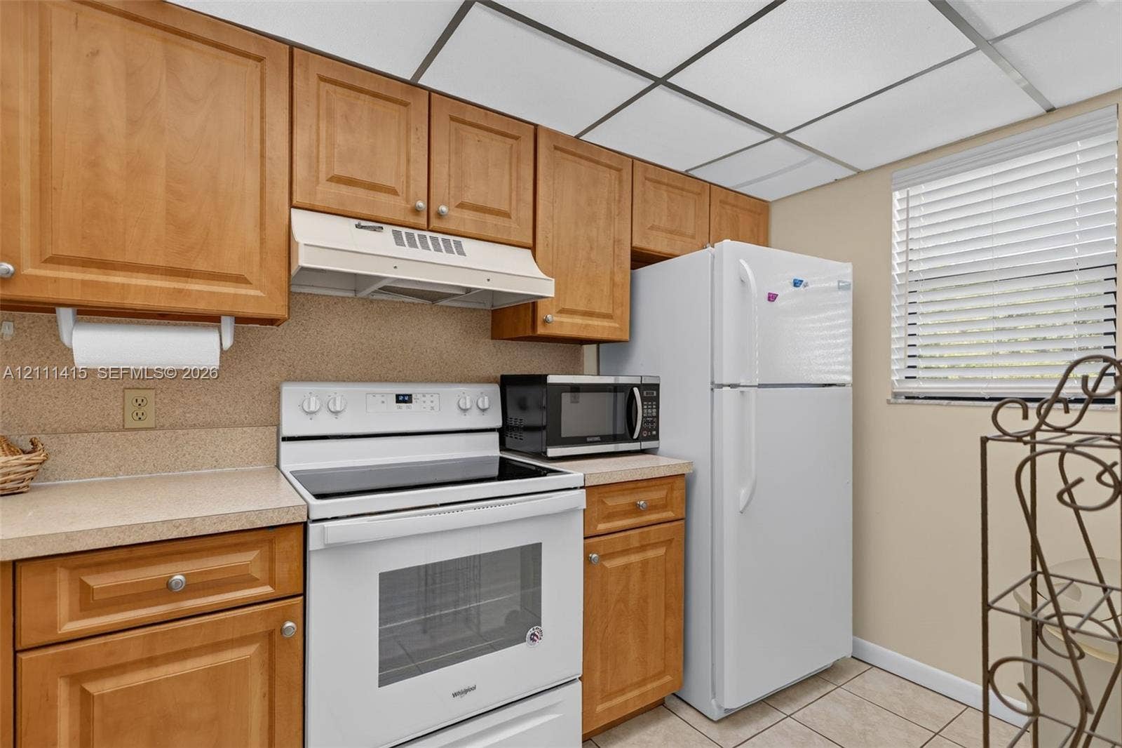 9423 S Ocean Drive, #80, Jensen Beach, FL 34957 Kitchen featuring medium-tone wood cabinetry, solid-surface countertops, white electric range with built-in range hood, white refrigerator, and tile flooring