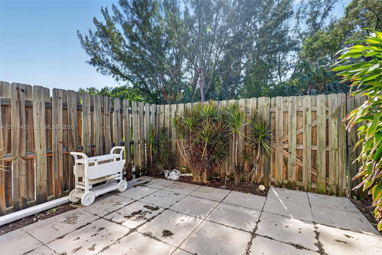 9423 S Ocean Drive, #80, Jensen Beach, FL 34957 Rear patio featuring concrete pavers, enclosed by a vertical wood-board fence with an integrated gate and perimeter landscaping