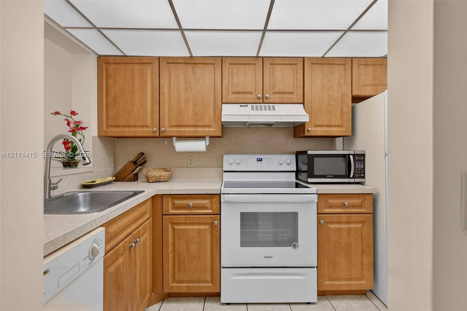 9423 S Ocean Drive, #80, Jensen Beach, FL 34957 Kitchen featuring solid wood cabinetry, light-toned composite countertops, a stainless steel undermount sink with a gooseneck faucet, white appliance suite, and a drop ceiling