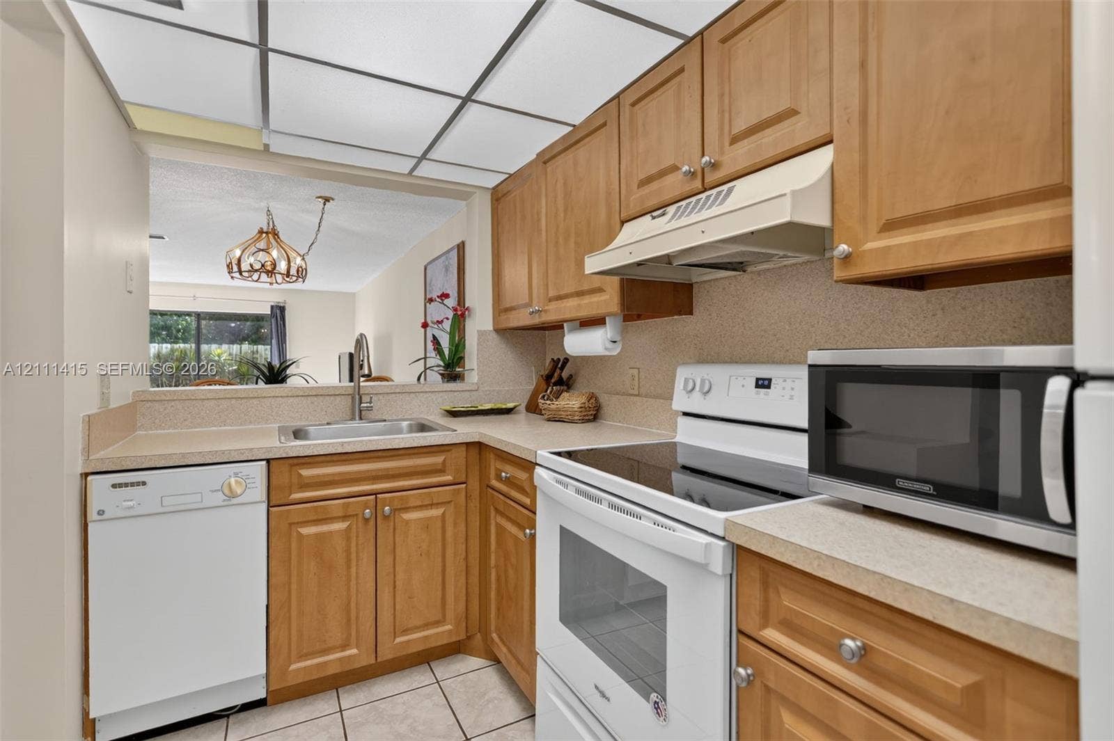 9423 S Ocean Drive, #80, Jensen Beach, FL 34957 Kitchen featuring shaker-style wood cabinetry, solid-surface countertops, a drop-in stainless steel sink, and a grid-pattern drop ceiling