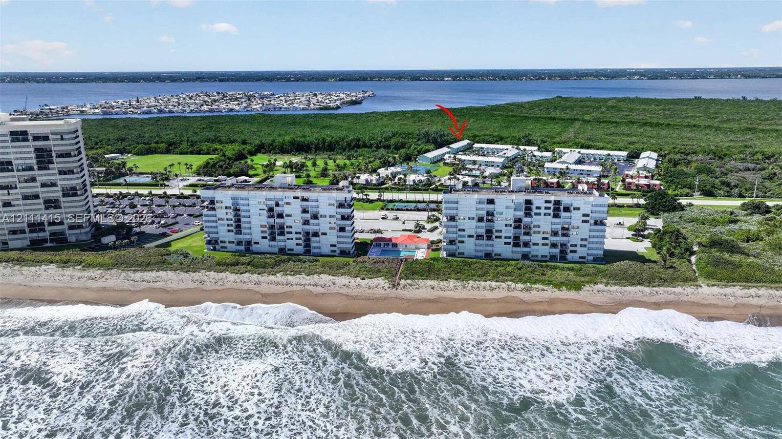 9423 S Ocean Drive, #80, Jensen Beach, FL 34957 Aerial perspective featuring multi-story residential buildings, direct oceanfront placement, paved parking facilities, and proximity to coastal vegetation and waterway