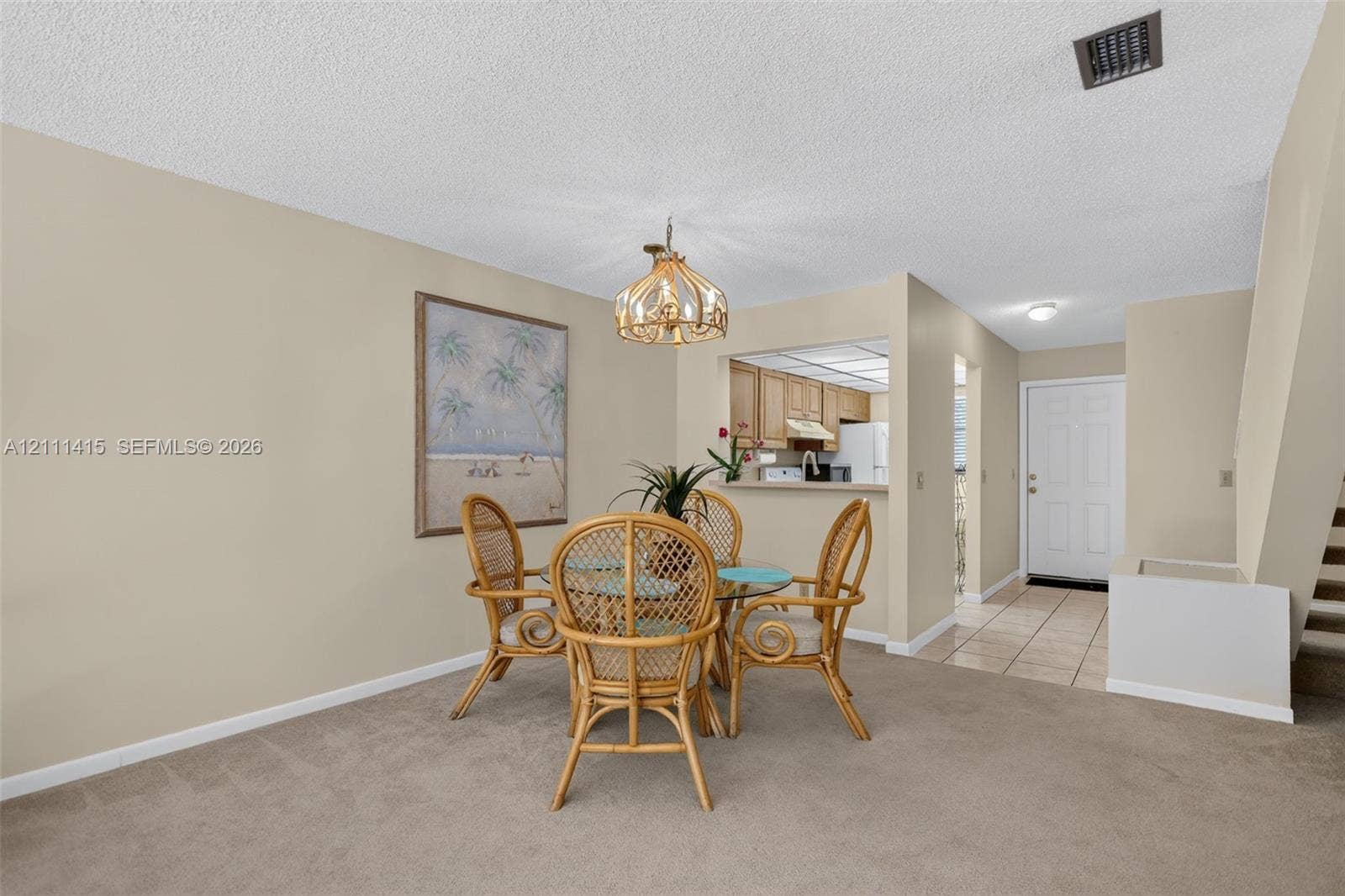 9423 S Ocean Drive, #80, Jensen Beach, FL 34957 Dining area featuring a decorative pendant light fixture, pass-through opening to the kitchen, neutral wall tones, and carpeted flooring