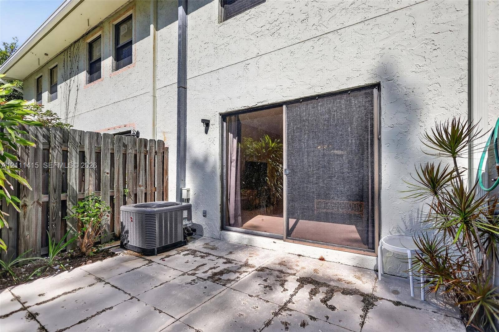 9423 S Ocean Drive, #80, Jensen Beach, FL 34957 Concrete patio with sliding glass door access, enclosed by a wood privacy fence and finished with a stucco exterior