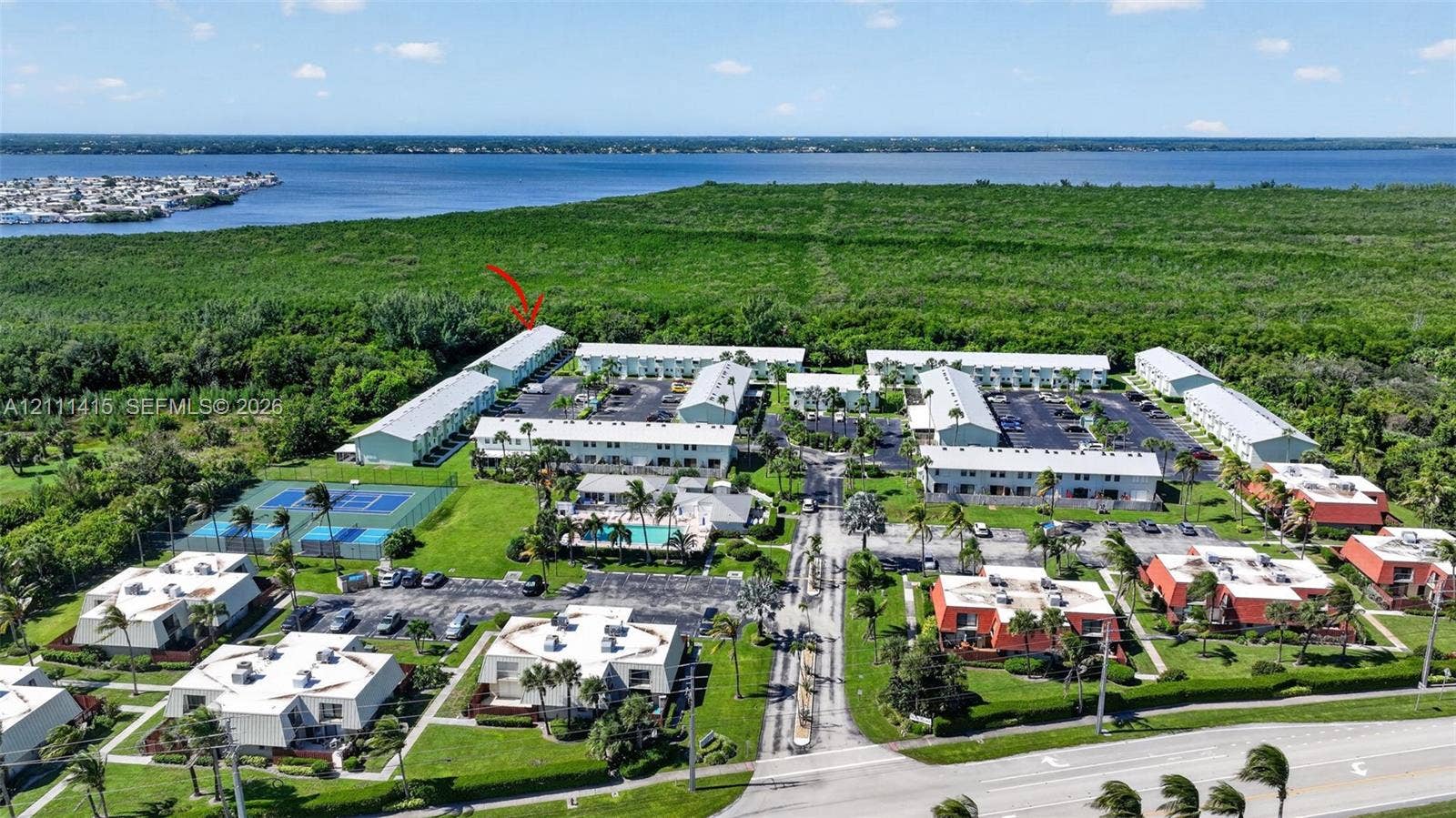 9423 S Ocean Drive, #80, Jensen Beach, FL 34957 Aerial perspective of a multi-building residential complex featuring paved parking areas, a swimming pool, and a tennis court