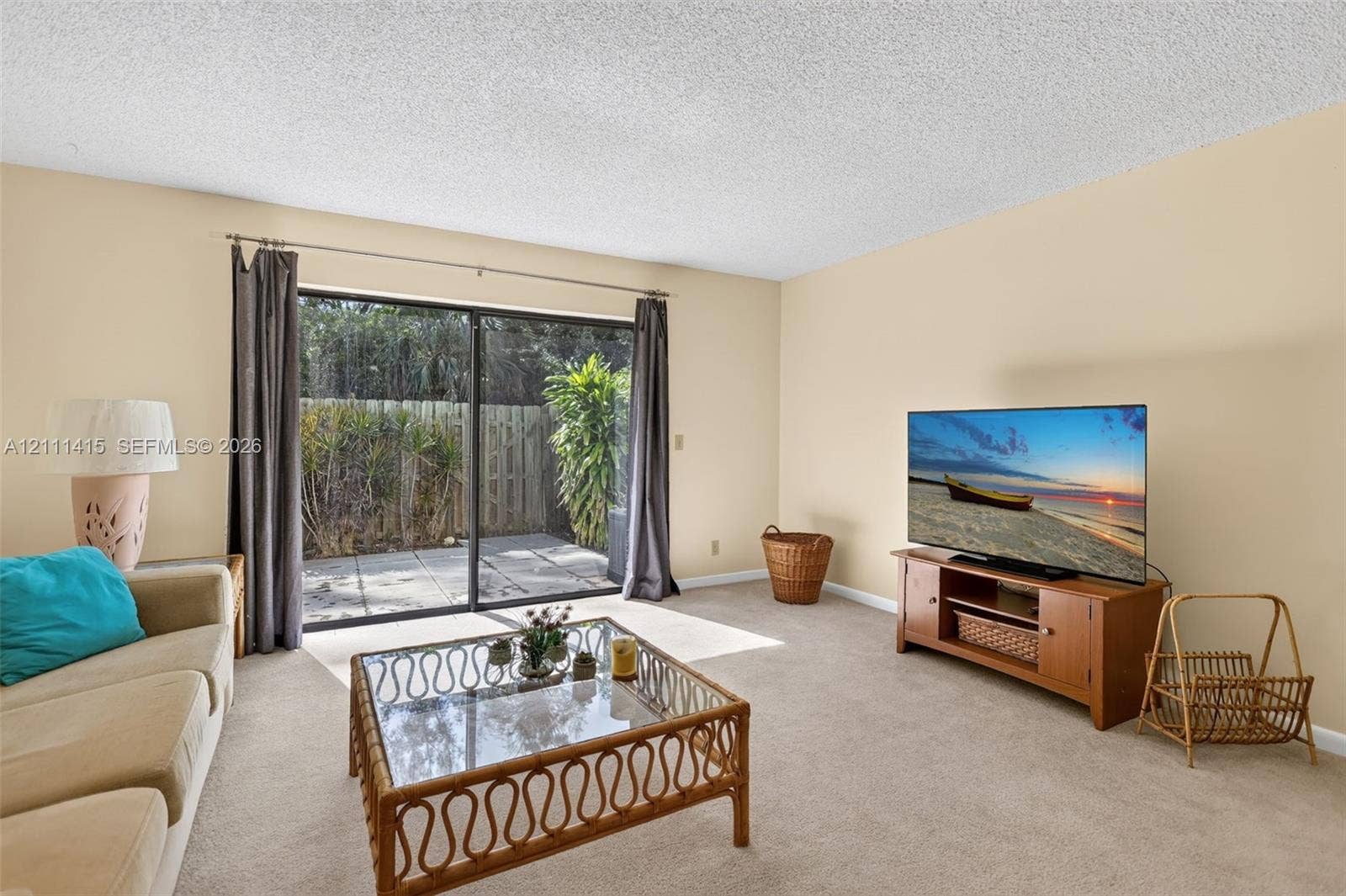 9423 S Ocean Drive, #80, Jensen Beach, FL 34957 Living space featuring neutral carpeting, a textured ceiling, and large sliding glass doors providing outdoor access to a paved patio area