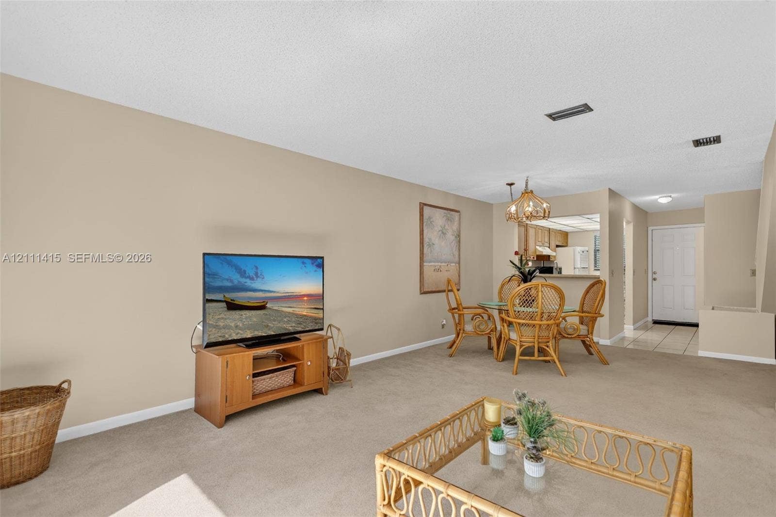 9423 S Ocean Drive, #80, Jensen Beach, FL 34957 Open-concept main living area featuring neutral wall paint, wall-to-wall carpeting, a decorative multi-bulb chandelier, and a pass-through kitchen opening