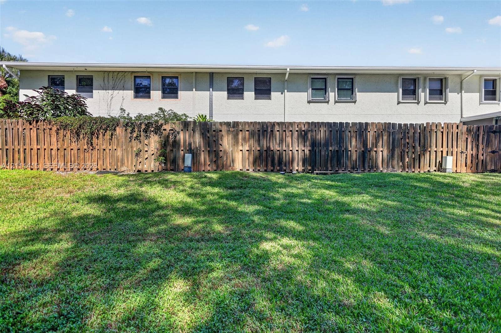9423 S Ocean Drive, #80, Jensen Beach, FL 34957 Expansive backyard featuring a manicured lawn, wood-slat privacy fencing, and a light-colored stucco exterior finish