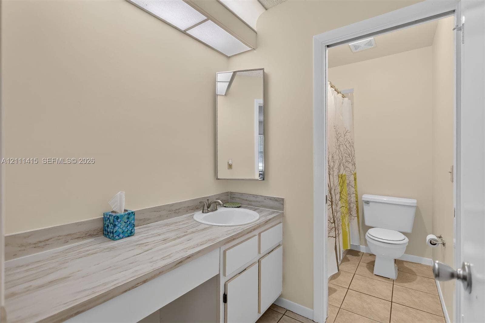 9423 S Ocean Drive, #80, Jensen Beach, FL 34957 Bathroom vanity featuring a wood-patterned countertop, integrated basin with metal hardware, white cabinetry, a rectangular wall-mounted mirror, and ceramic tile flooring