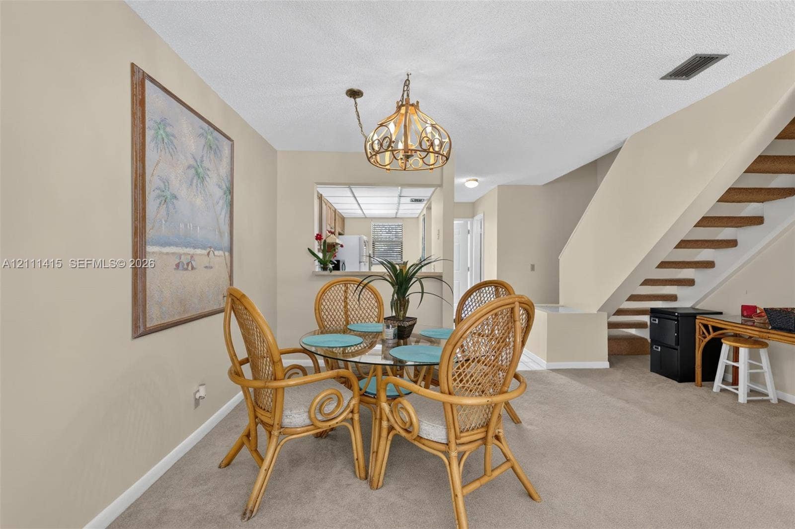 9423 S Ocean Drive, #80, Jensen Beach, FL 34957 Neutral-toned dining area featuring a tiered metal chandelier, staircase with open-riser wood treads, and a pass-through window looking into the kitchen