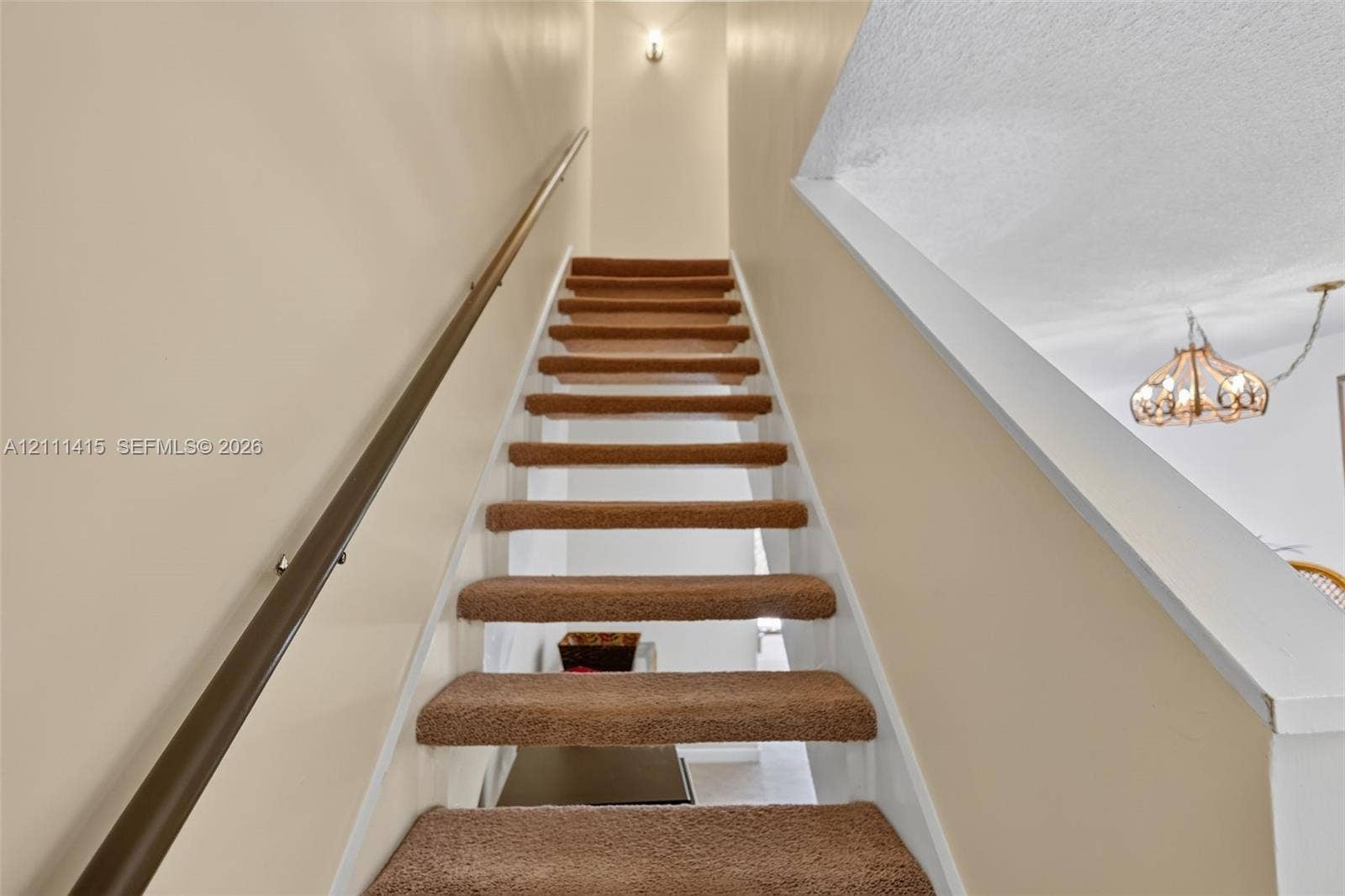 9423 S Ocean Drive, #80, Jensen Beach, FL 34957 Staircase featuring wall-to-wall carpeted treads, a solid wood handrail with metallic mounting hardware, and a semi-flush mount ceiling light fixture