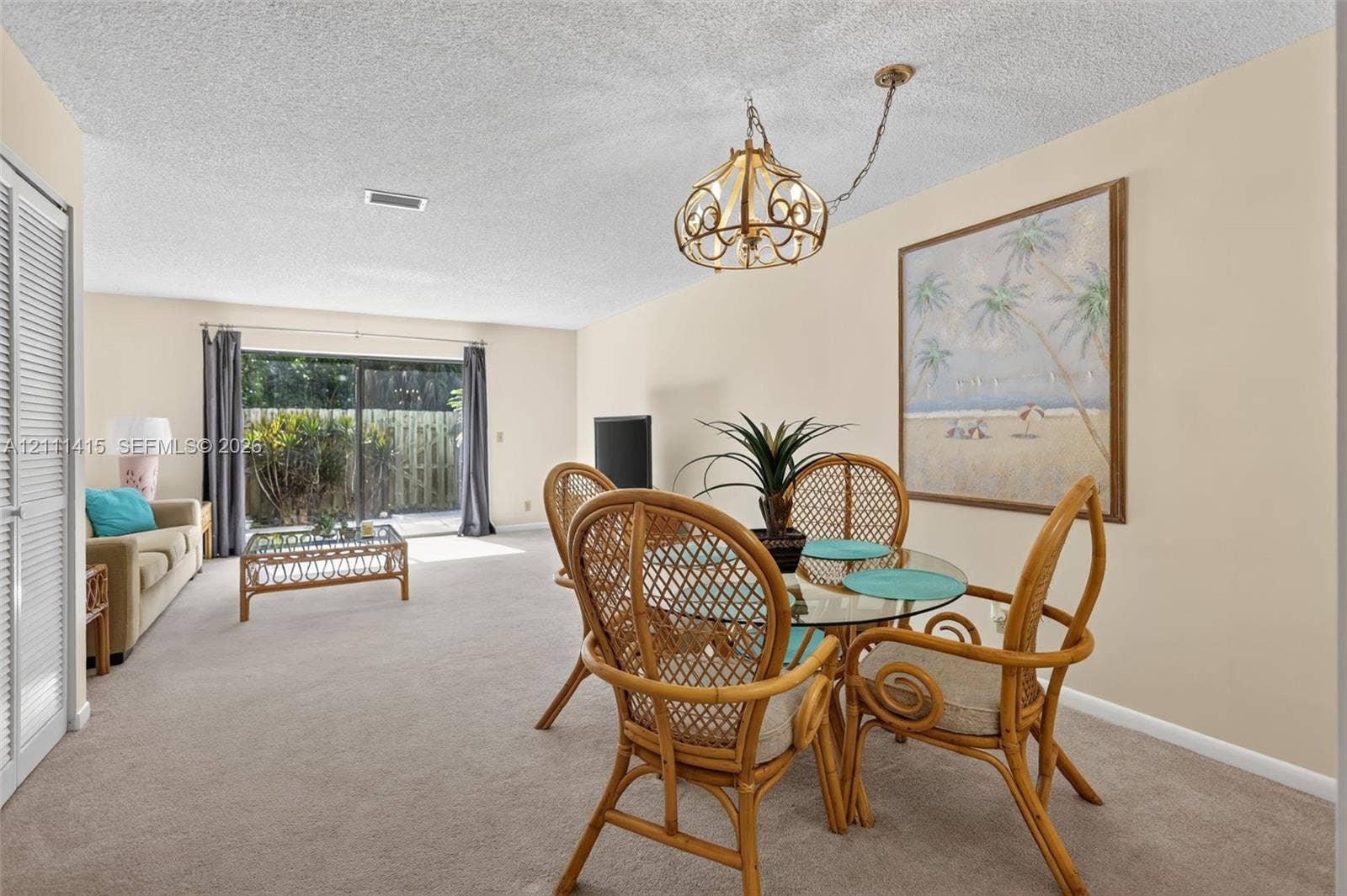 9423 S Ocean Drive, #80, Jensen Beach, FL 34957 Open-concept interior featuring neutral wall tones, wall-to-wall carpeting, an ornate metal chandelier, and sliding glass doors providing outdoor access