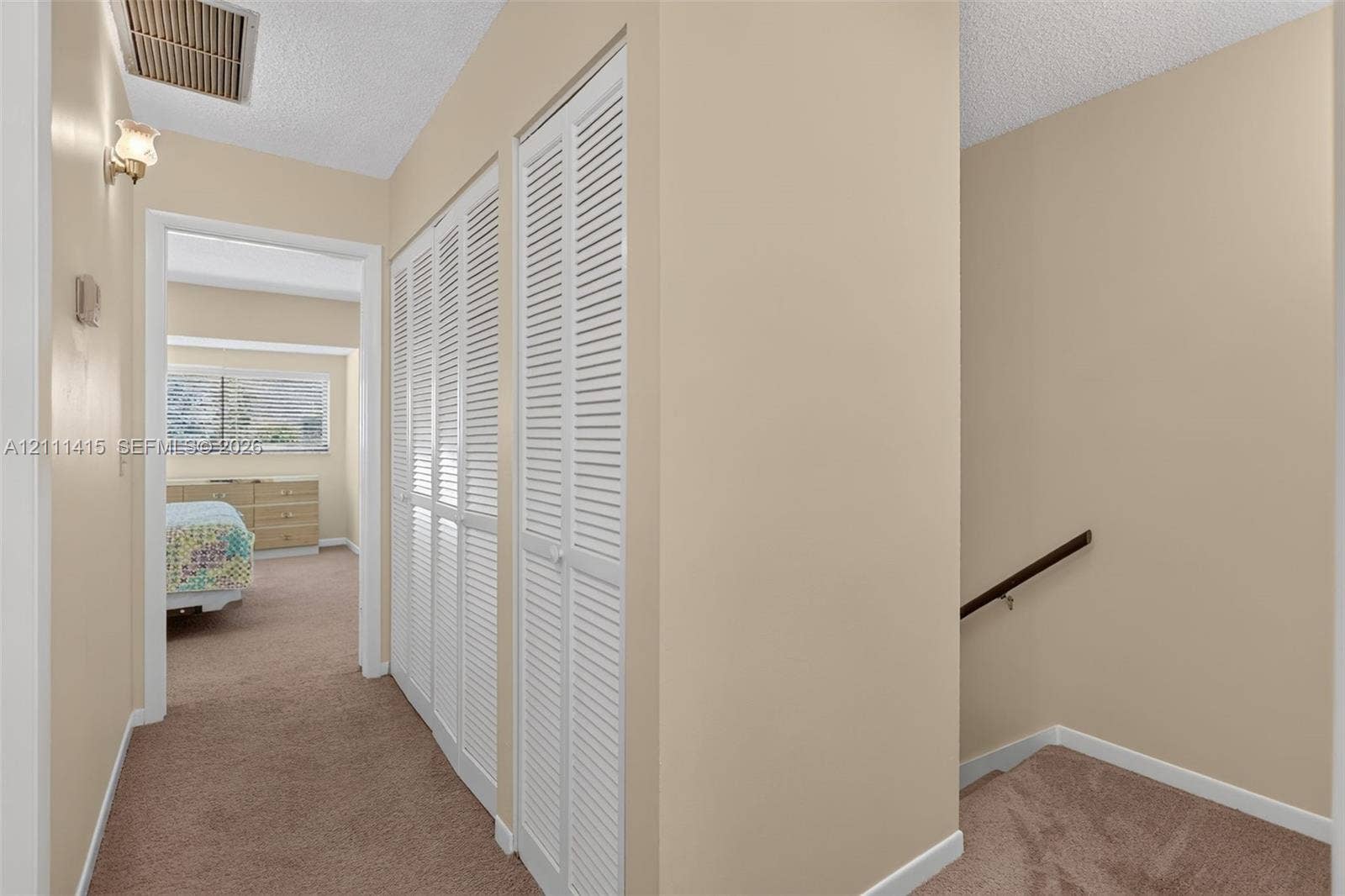 9423 S Ocean Drive, #80, Jensen Beach, FL 34957 Hallway featuring dual white louvered closet doors, carpeted flooring, and a wall-mounted handrail along the stairwell