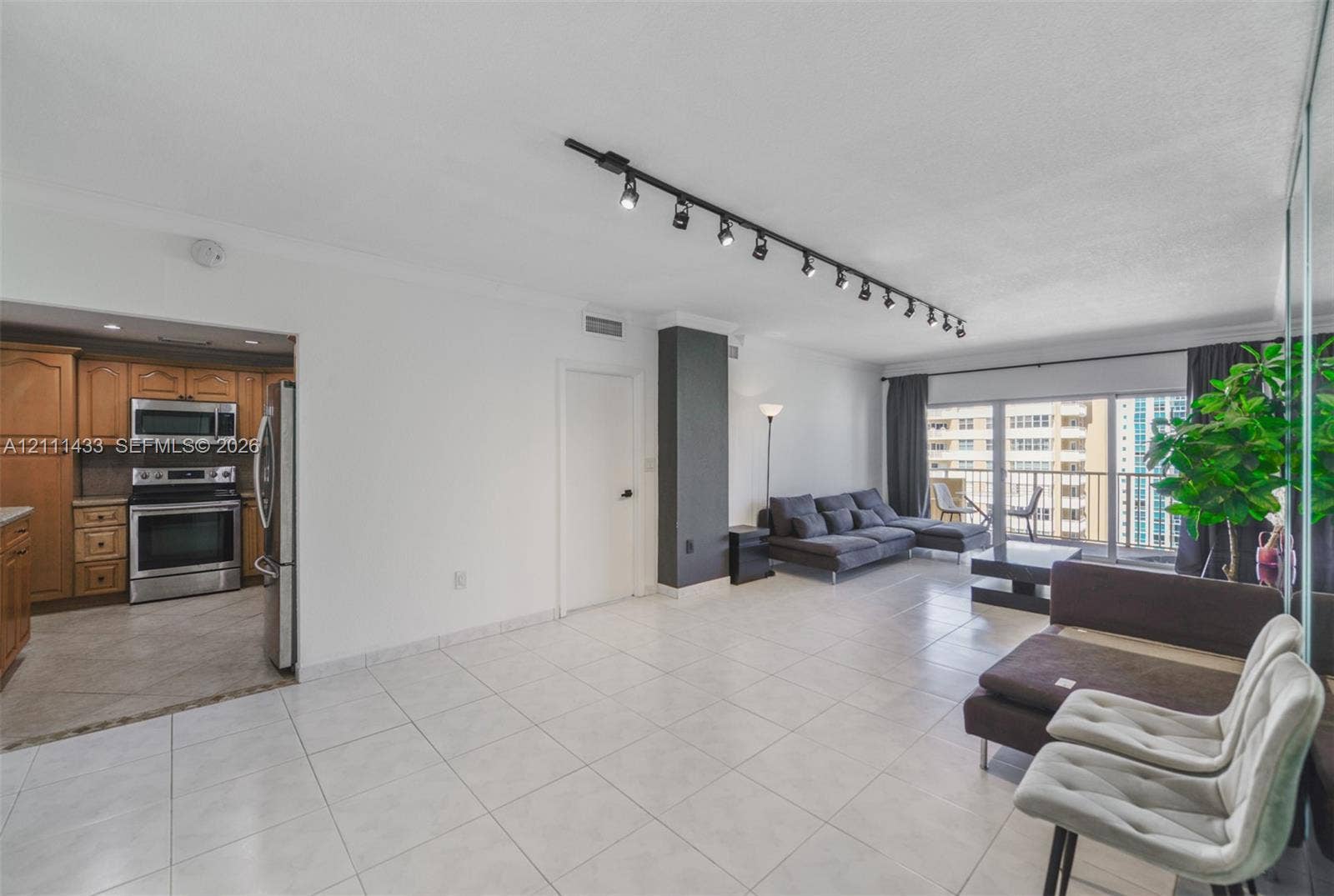 Open-concept interior featuring large-format ceramic tile flooring, track lighting, a full-height mirrored wall, and stainless steel kitchen appliances