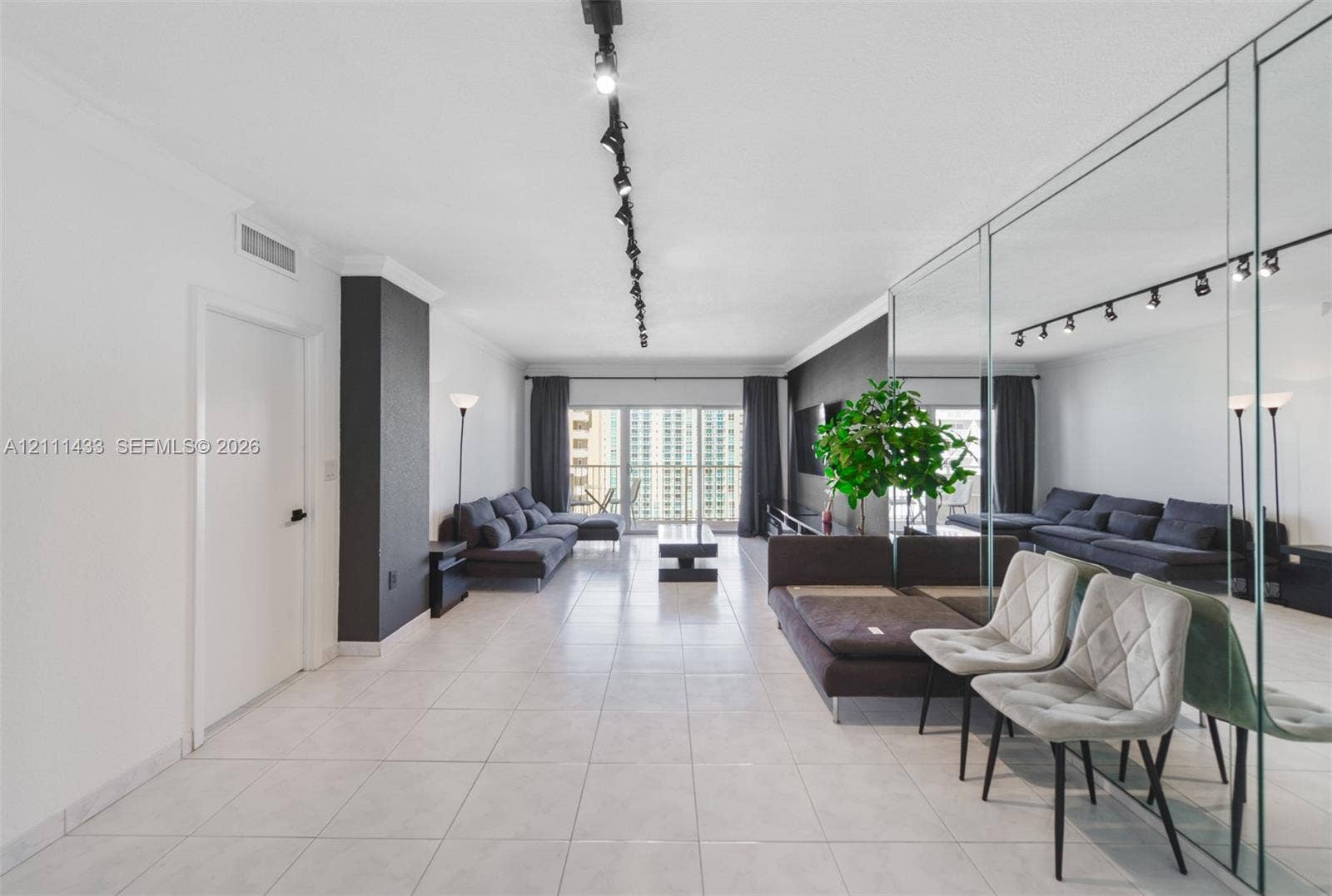 Living area featuring large-format tile flooring, a floor-to-ceiling mirrored wall, adjustable track lighting, and sliding glass doors with access to an exterior balcony