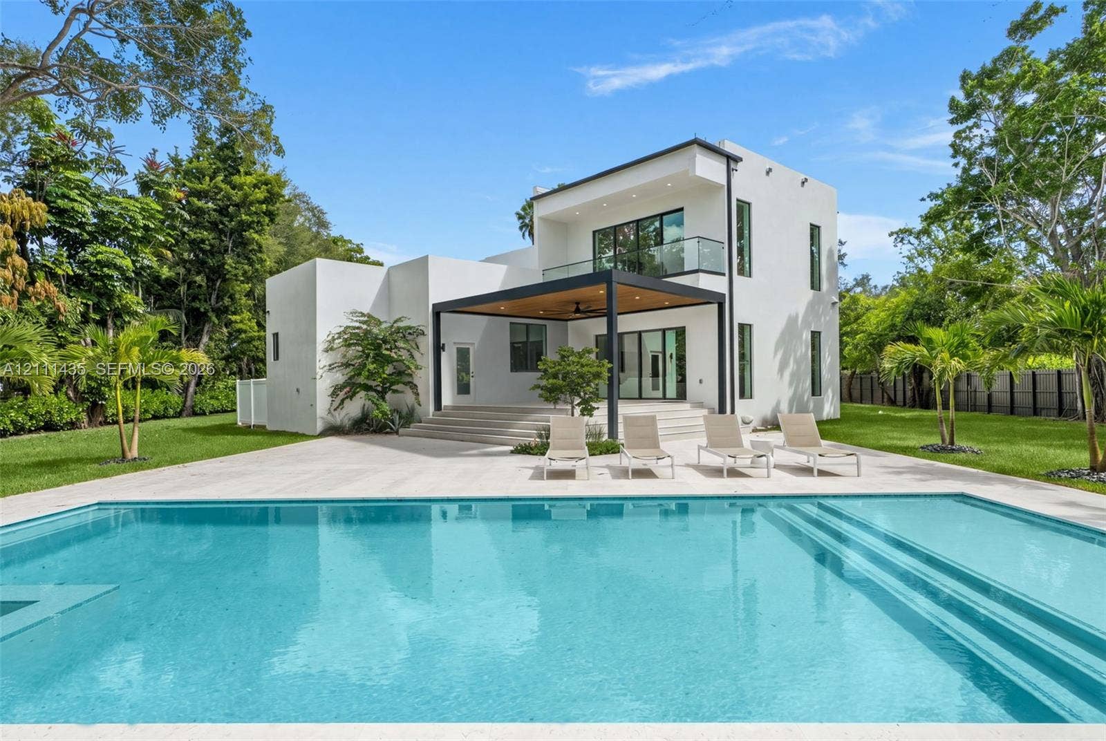 9530 SW 95th Court, Miami, FL 33176 Modern two-story residence featuring a smooth stucco exterior, expansive concrete patio, built-in swimming pool with step entry, and a covered pavilion with recessed lighting