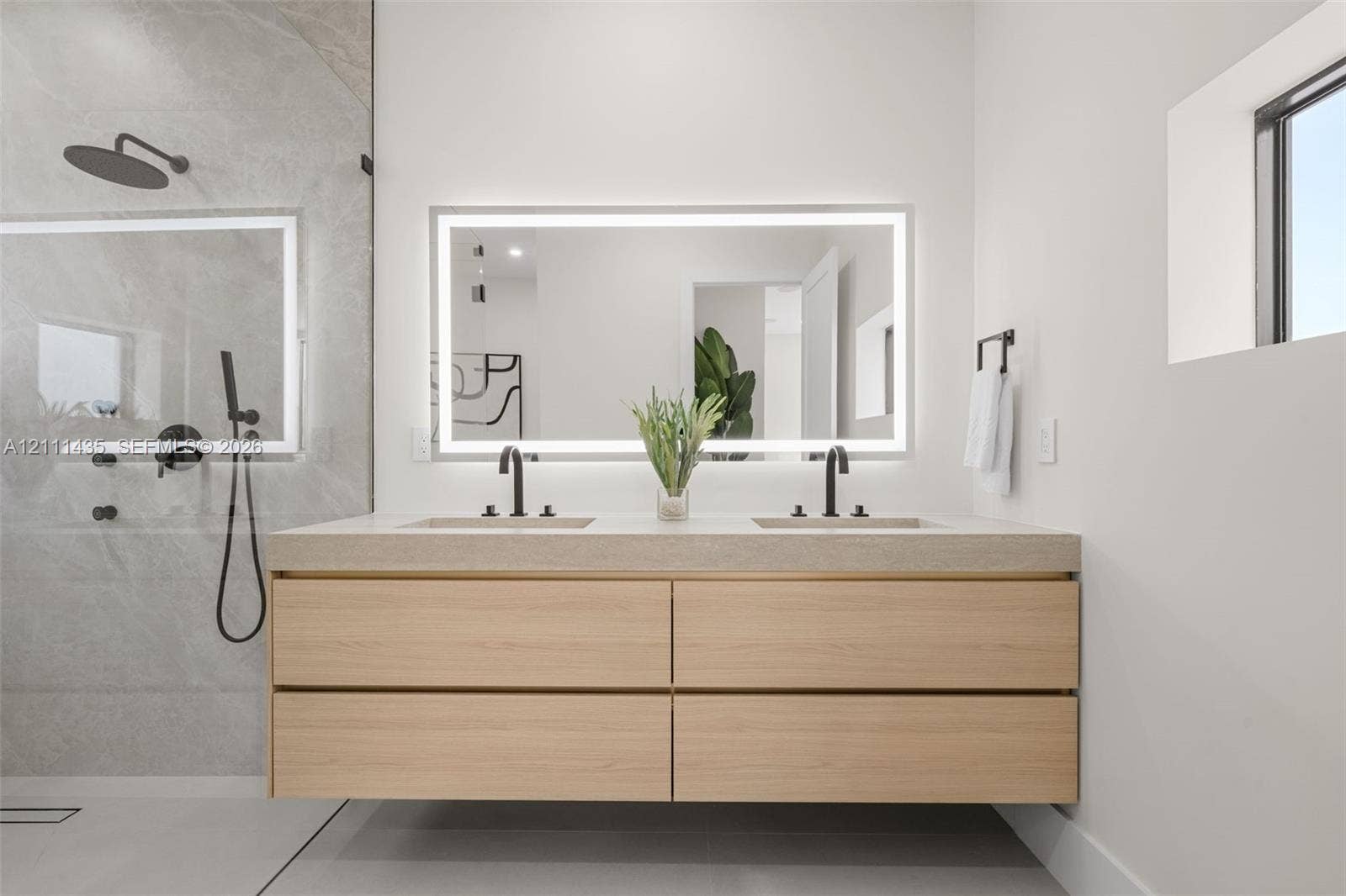 9530 SW 95th Court, Miami, FL 33176 Floating wood-finish vanity with dual sinks, stone-surface countertop, LED-backlit mirror, and matte black fixtures, paired with a walk-in shower featuring large-format wall tile and matte black shower hardware