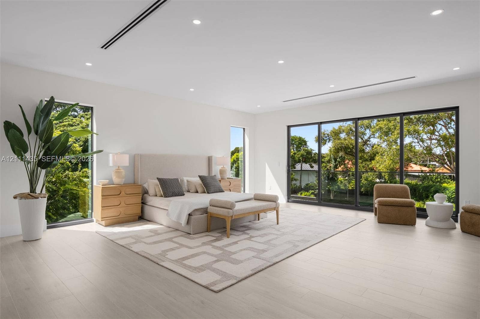 9530 SW 95th Court, Miami, FL 33176 Spacious interior featuring light-toned wood-finish flooring, recessed lighting, full-height windows, and floor-to-ceiling sliding glass doors with dark metal frames