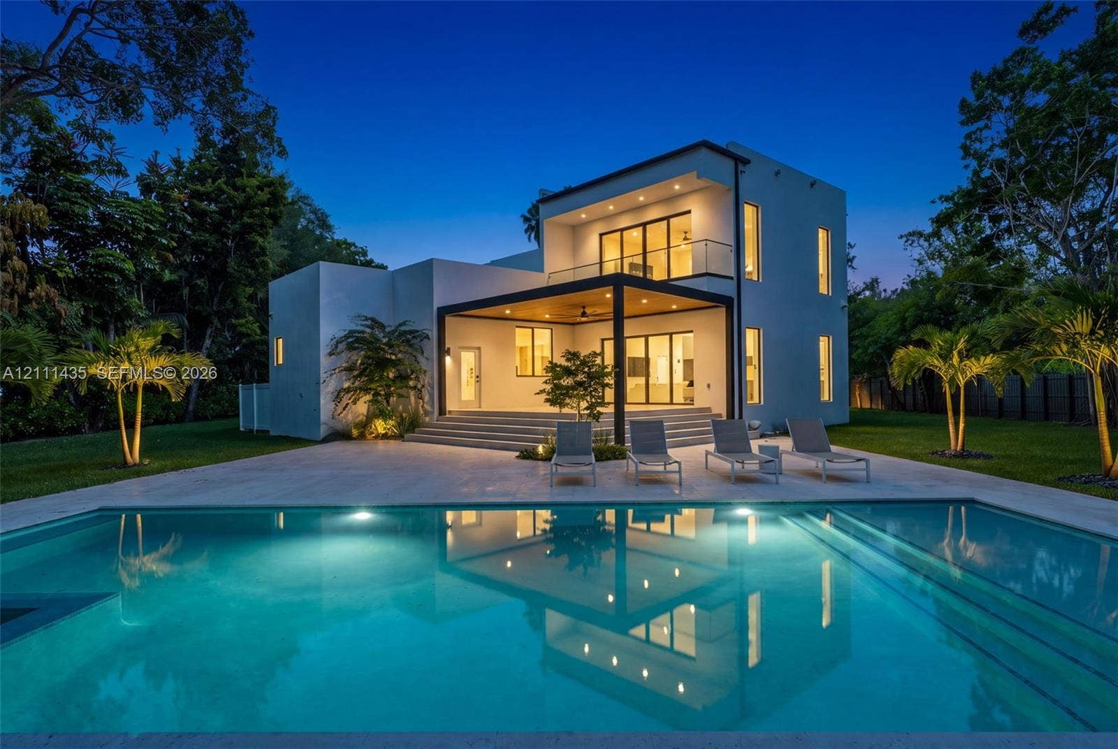 9530 SW 95th Court, Miami, FL 33176 Modern two-story residence featuring a smooth stucco exterior, a covered patio with recessed lighting, a second-level balcony with a glass railing, and an inground swimming pool with stone decking