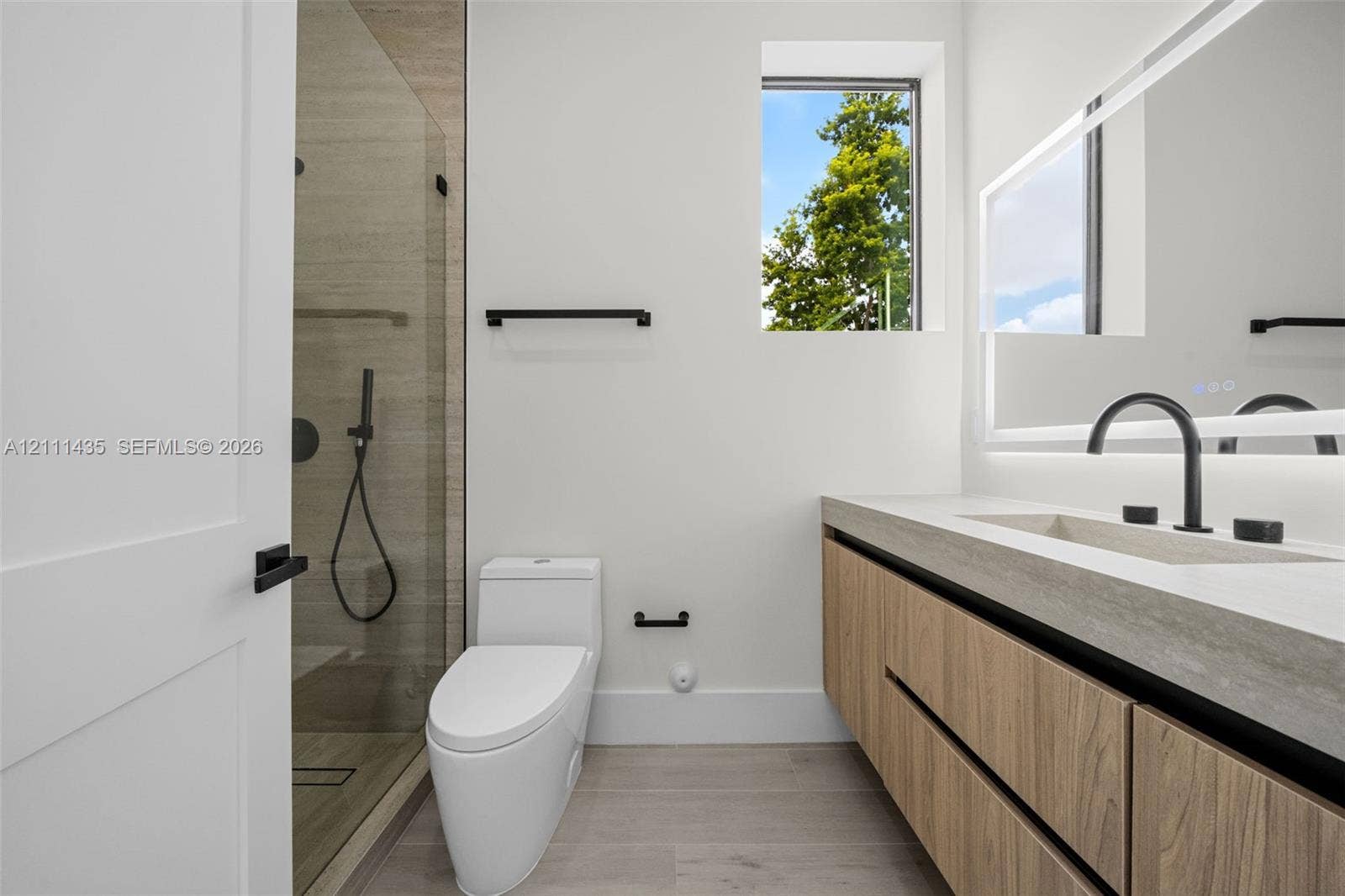 9530 SW 95th Court, Miami, FL 33176 Floating vanity with wood-finish cabinetry, rectangular integrated sink, matte black hardware, glass-enclosed shower, and illuminated mirror