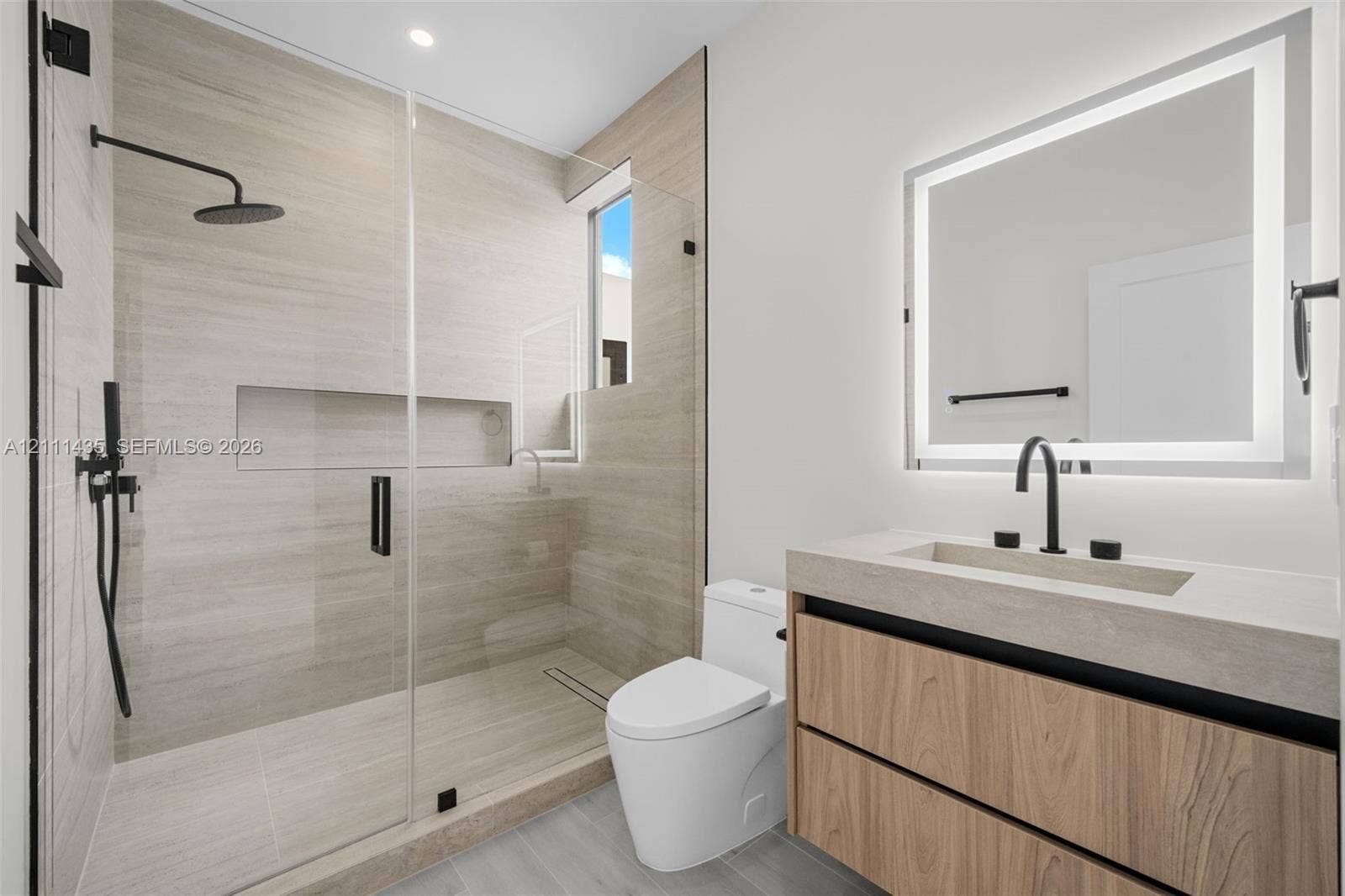 9530 SW 95th Court, Miami, FL 33176 Bathroom featuring a floating wood-finish vanity, integrated stone-composite countertop, illuminated mirror, walk-in shower with floor-to-ceiling tile, and matte black fixtures