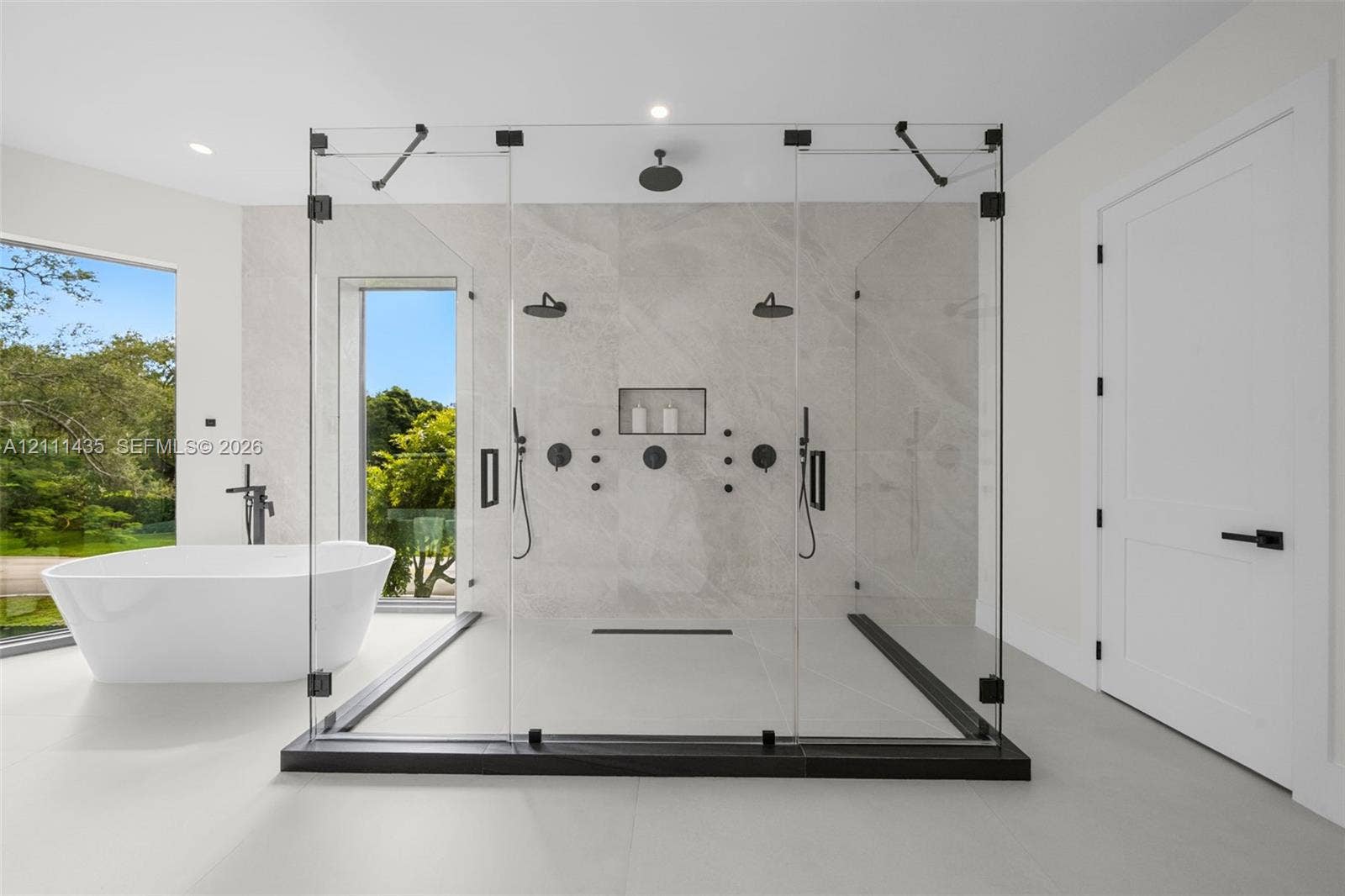 9530 SW 95th Court, Miami, FL 33176 Walk-in glass-enclosed shower featuring dual shower heads, a built-in recessed niche, and stone-finish wall tile, paired with a freestanding soaking tub and matte black fixtures