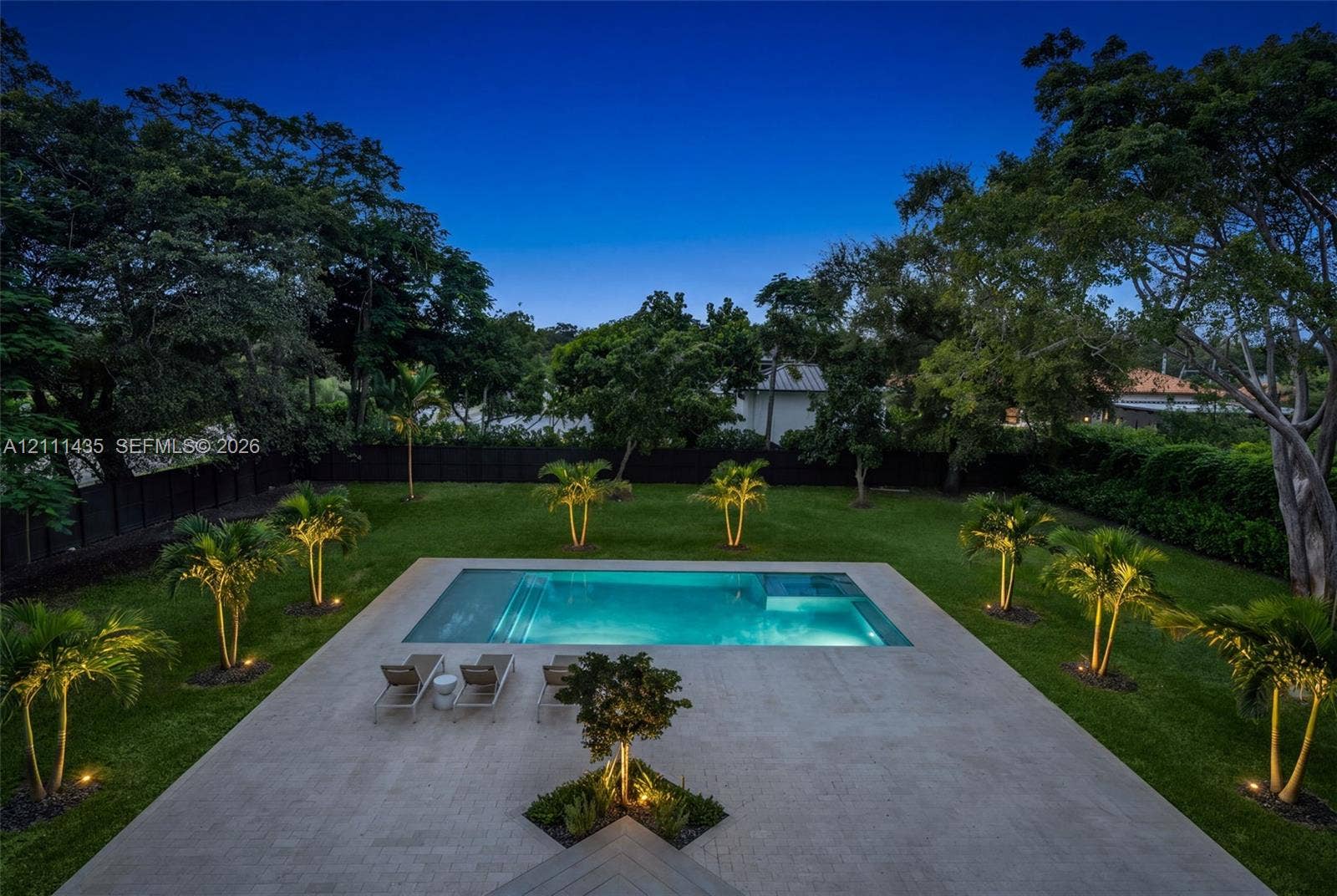 9530 SW 95th Court, Miami, FL 33176 In-ground swimming pool featuring a tanning ledge, light-toned stone patio, manicured lawn, perimeter fencing, and established palms